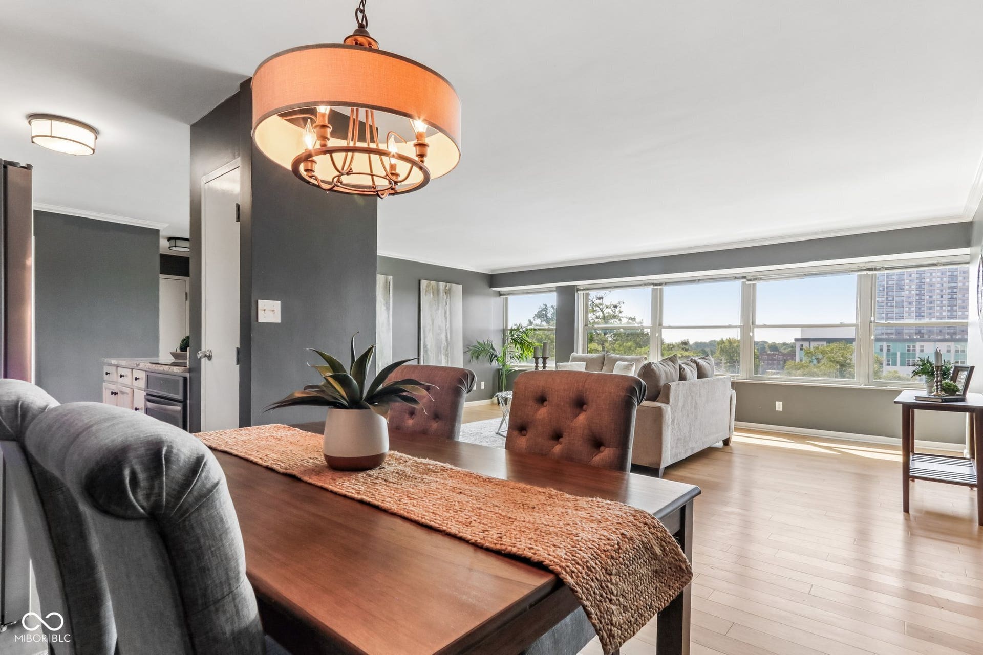Expansive windows, light wood-finish flooring, recessed ceiling lighting, and a drum pendant light fixture