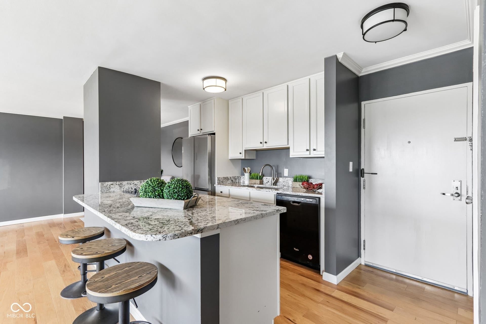 Kitchen area featuring white cabinetry, granite countertops, stainless steel refrigerator, black dishwasher, and wood-finish flooring
