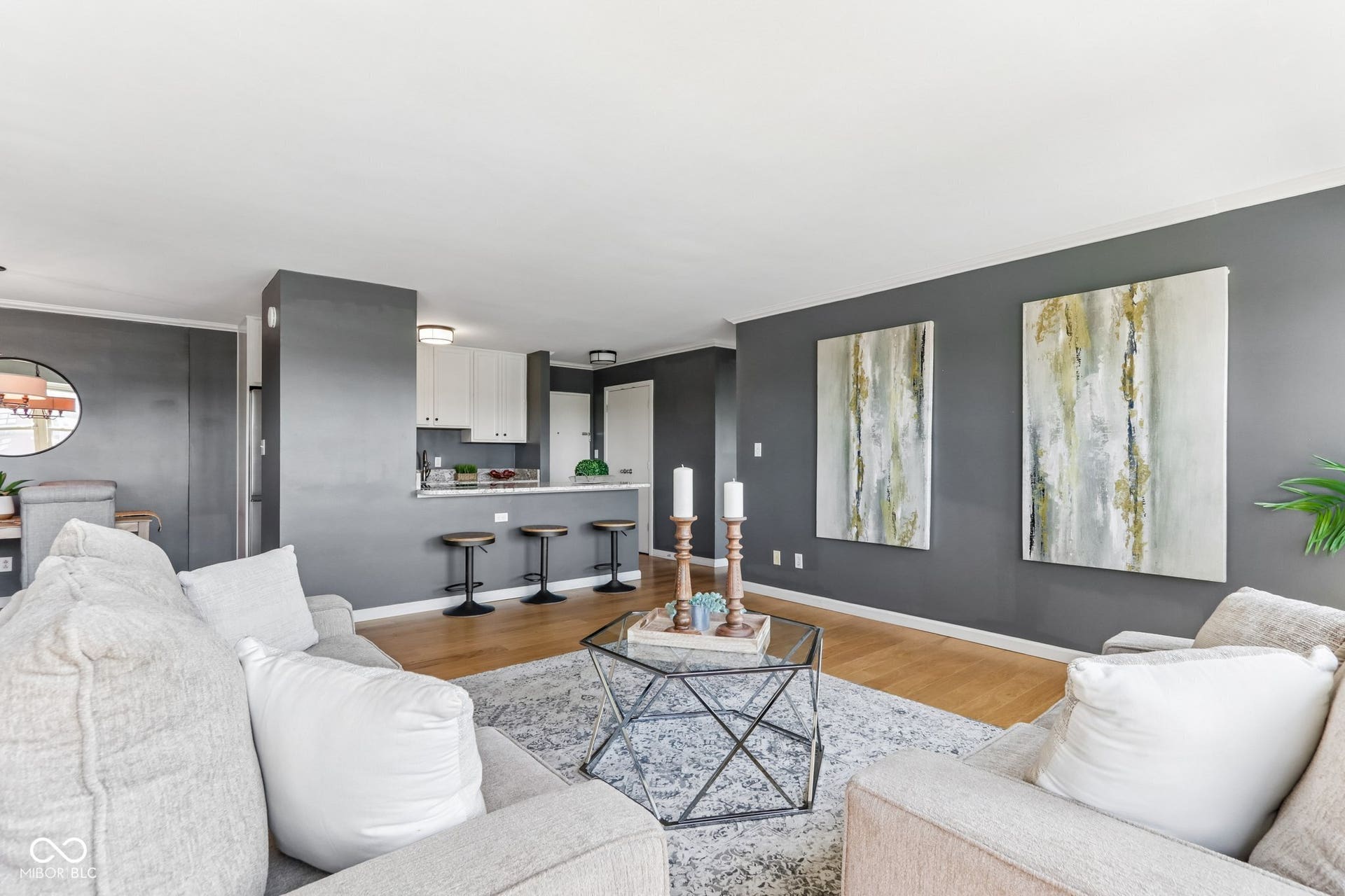 Open-concept living space with wood-finish flooring, white overhead lighting, and a kitchen island with seating