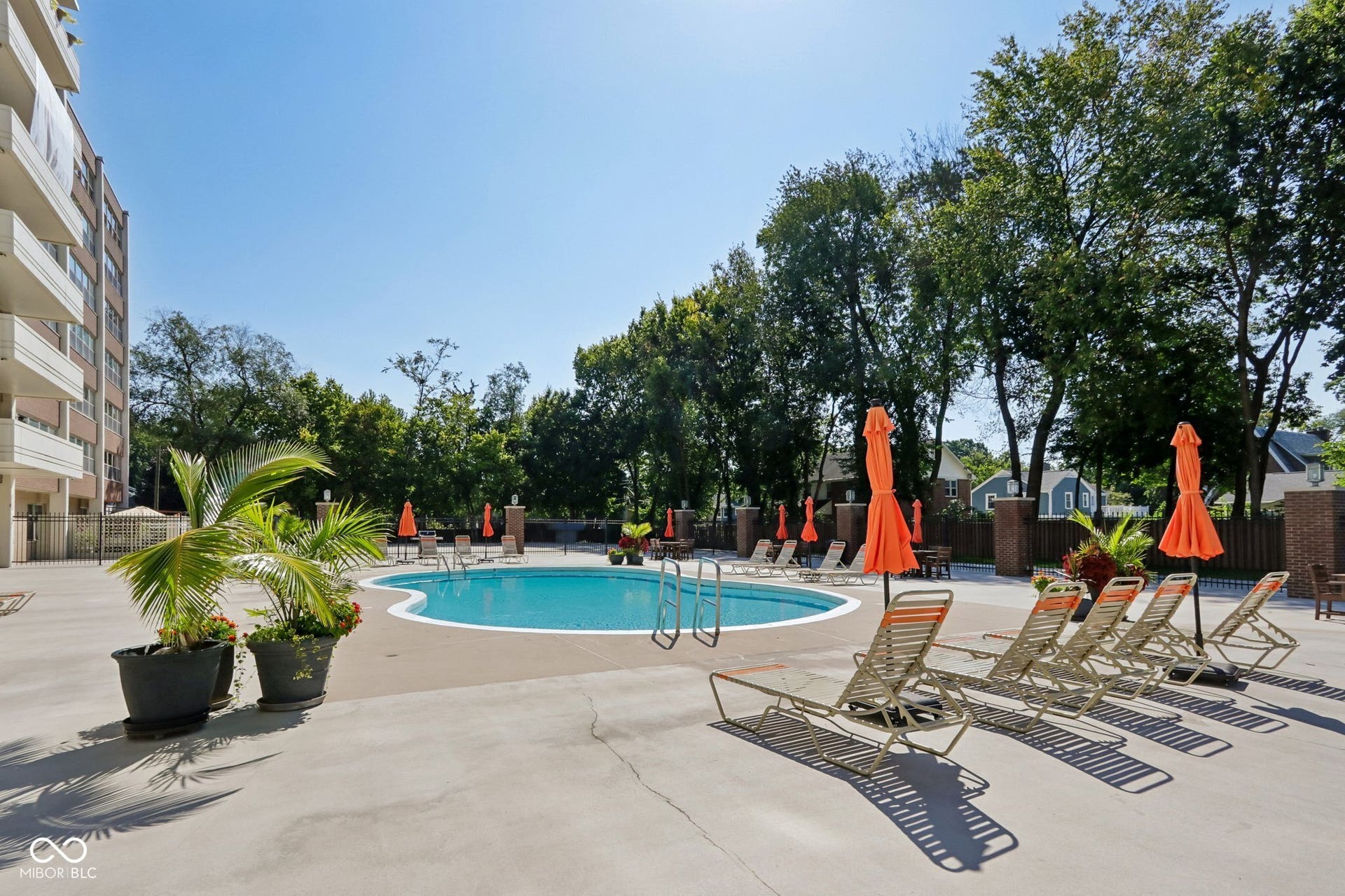 Outdoor swimming pool with integrated steps, surrounding concrete decking, brick fencing, and mature trees
