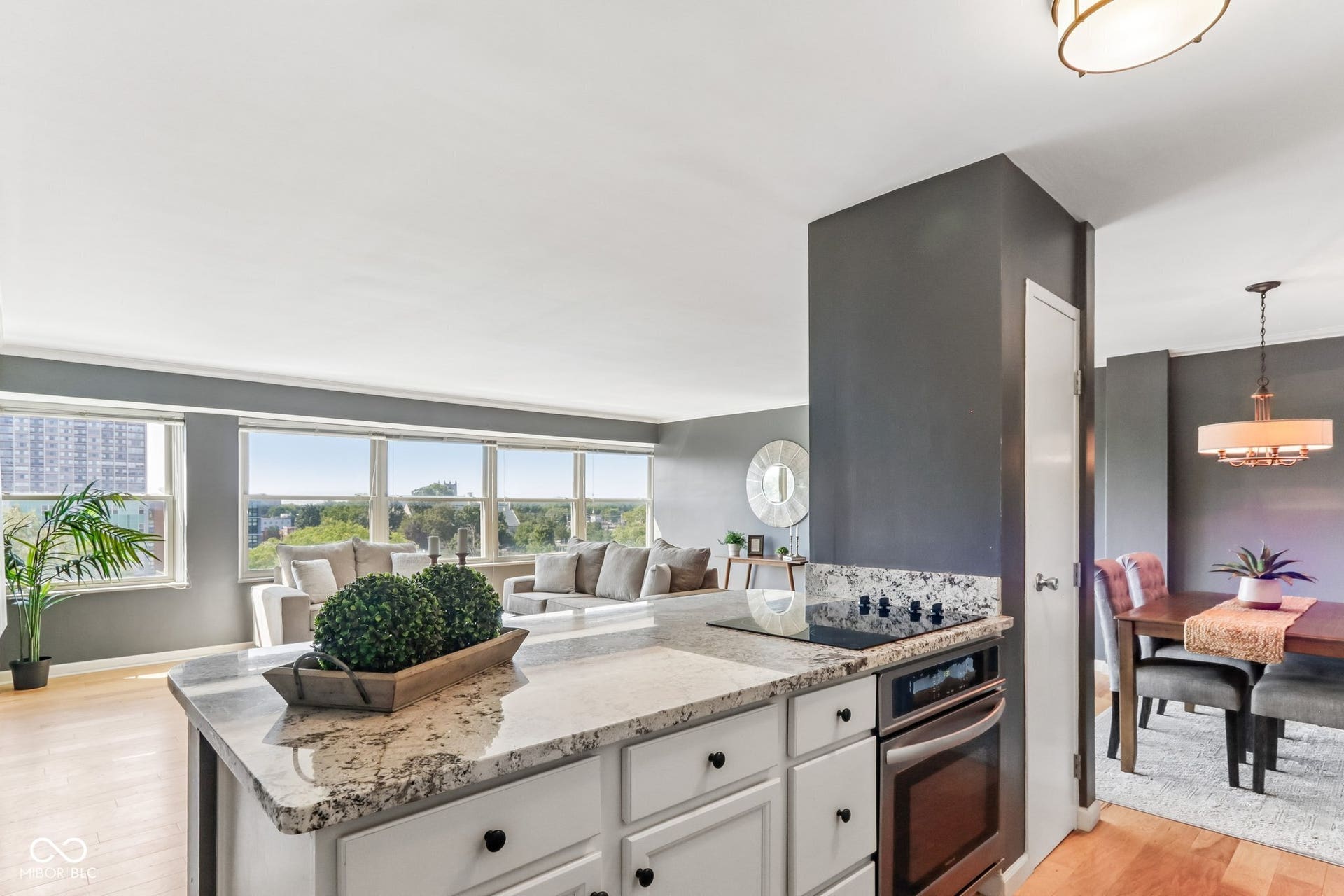 Kitchen island with light-toned countertop and built-in cooktop, integrated wall oven, white cabinetry, and dark hardware