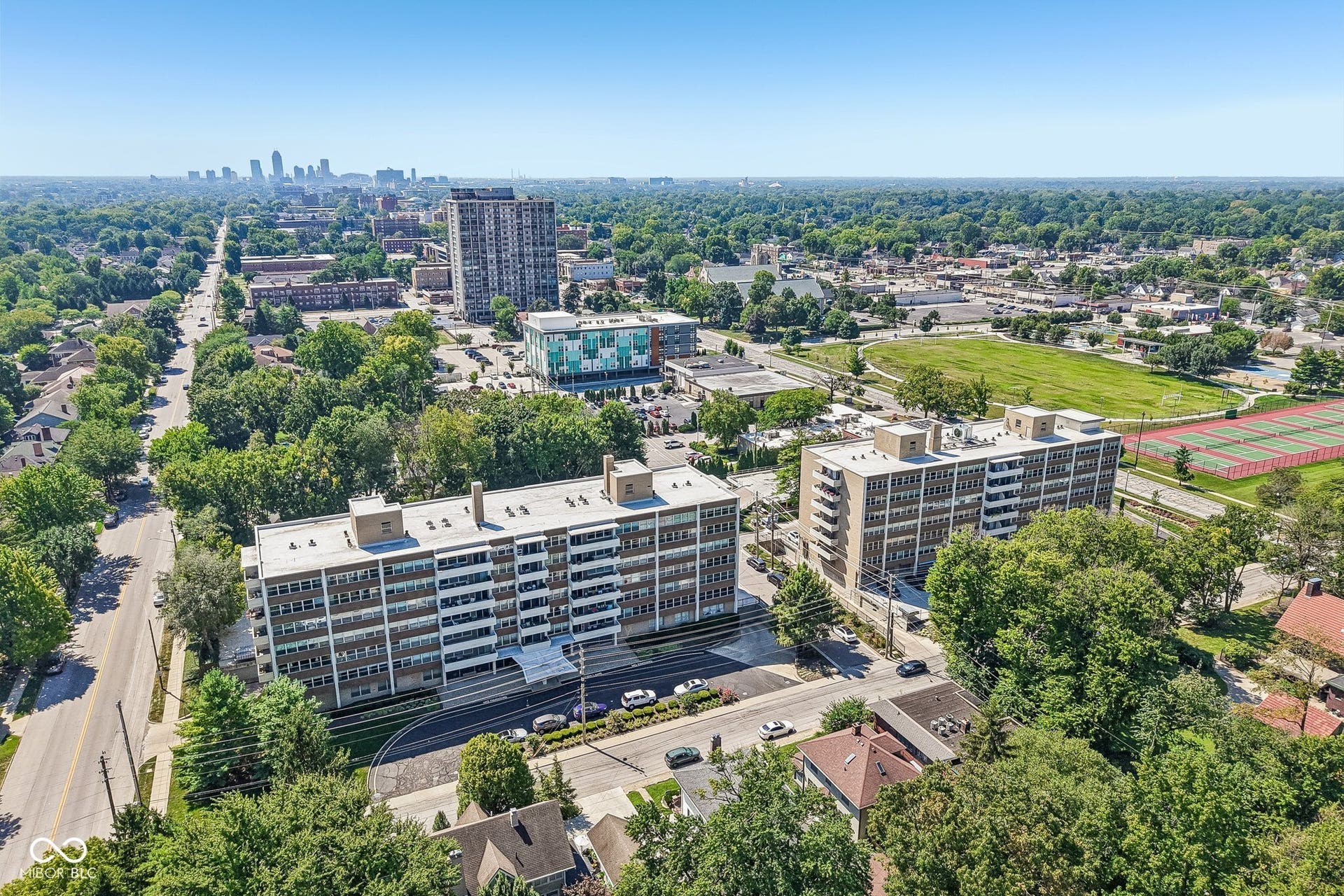 Aerial perspective showcasing multiple residential buildings, verdant tree canopy, and distant urban skyline