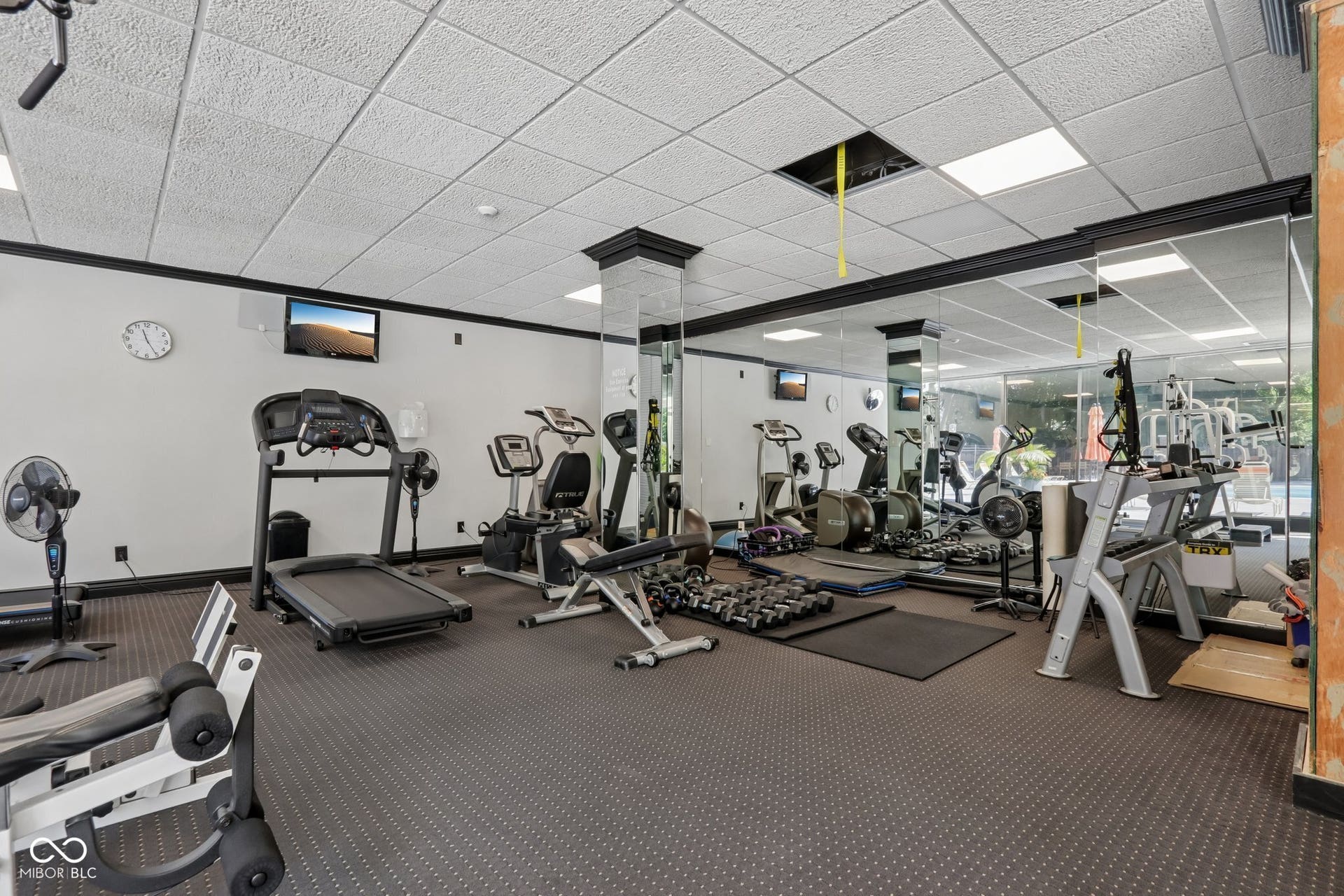 located in the East Building: Fitness area featuring a textured ceiling, mirrored walls, cardio equipment, and strength training machines