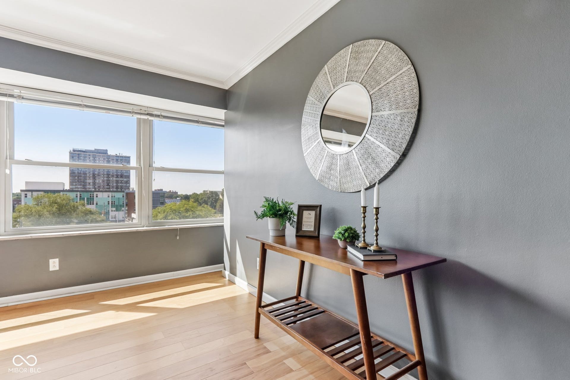 Expansive window providing abundant natural light, light wood-finish flooring, and a neutral wall color