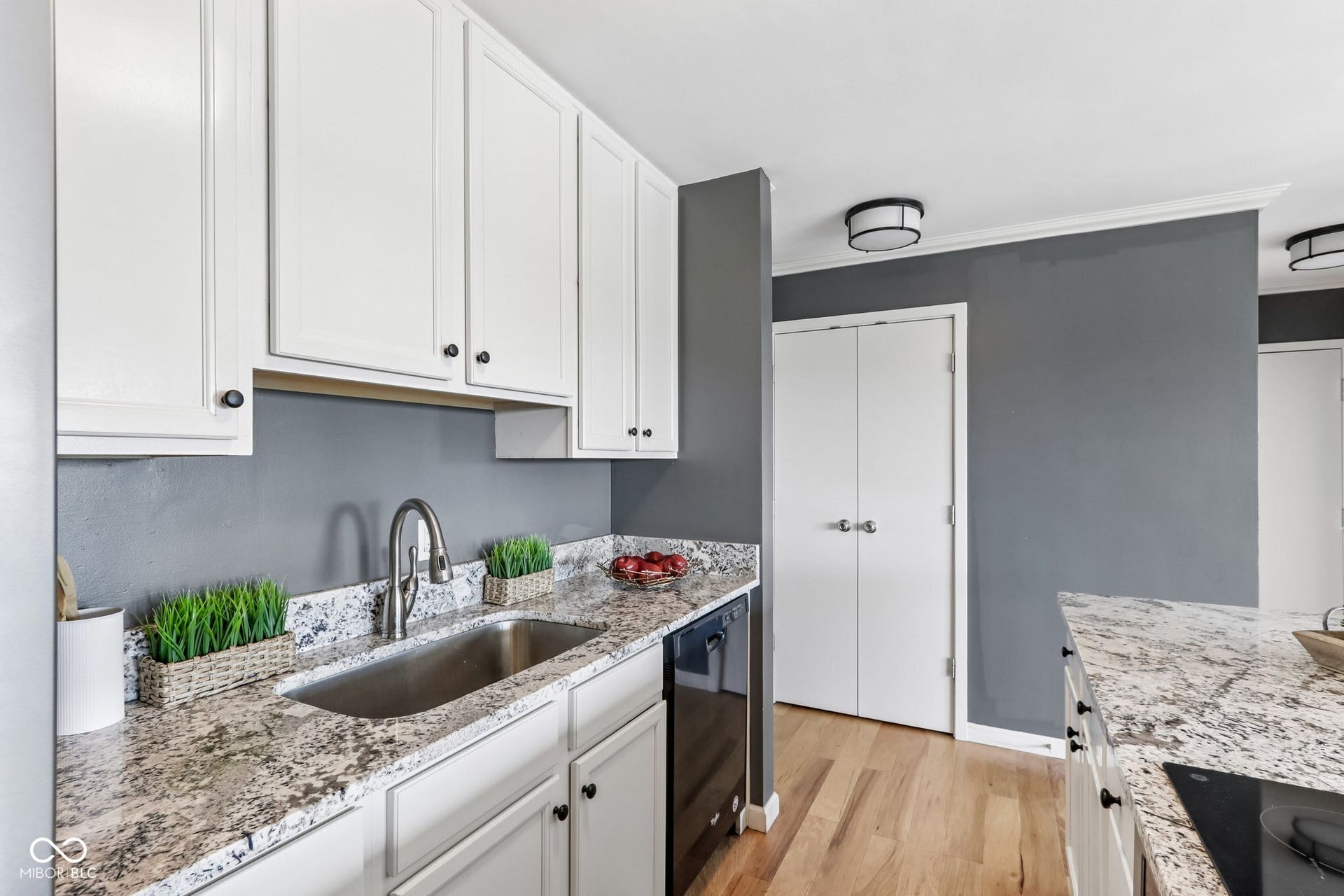 White cabinetry with black hardware, stainless steel sink with a gooseneck faucet, light-toned wood-finish flooring, and white double-fold doors