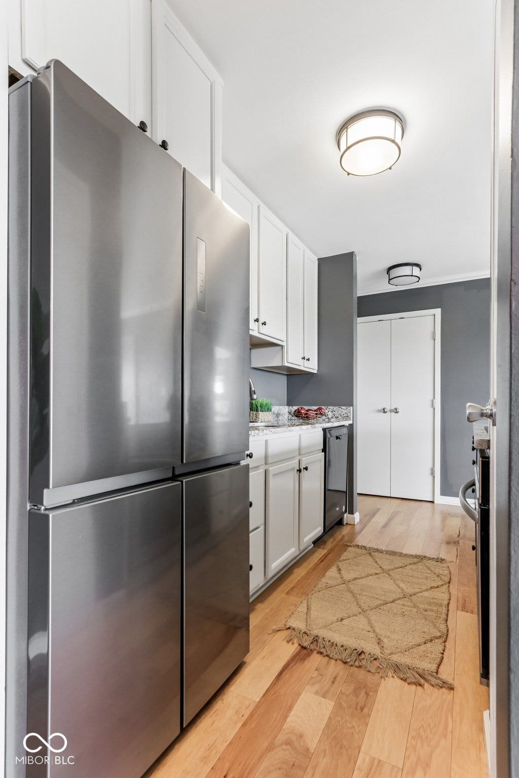 Stainless steel refrigerator, wood-finish flooring, white cabinetry, dark countertops, and ceiling-mounted lighting fixtures