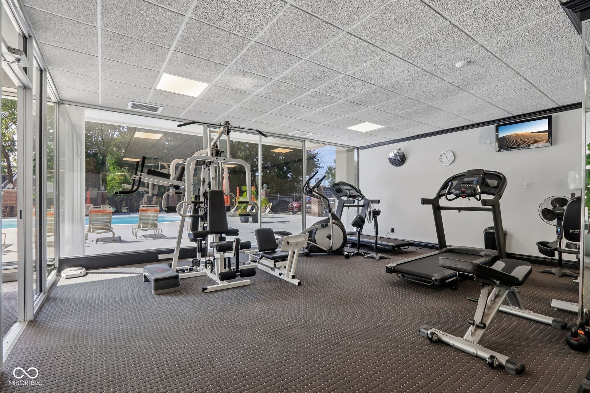 located in the East building: Fitness area featuring full-height windows, textured ceiling, wall-mounted television, and resilient flooring
