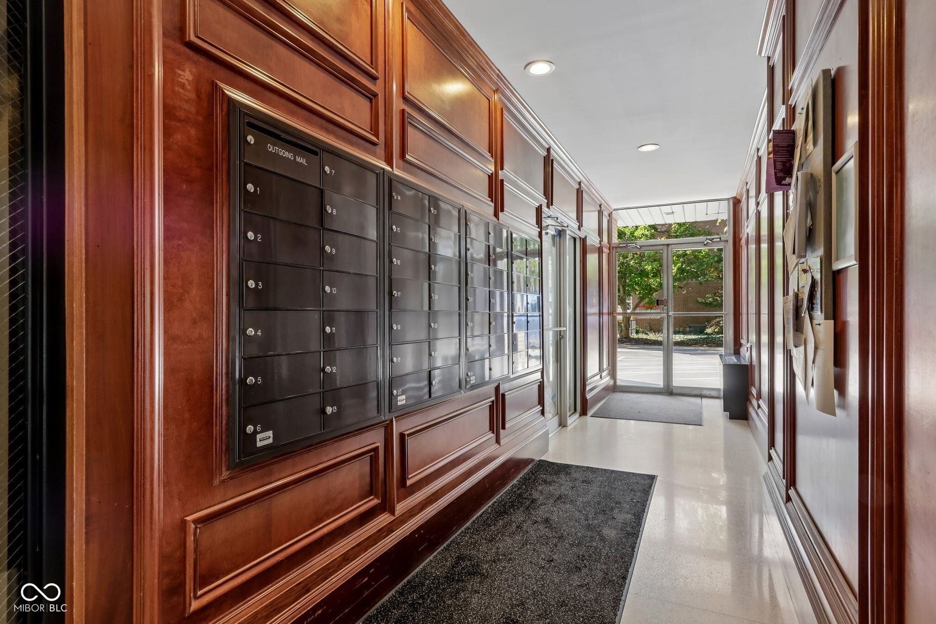 Mail delivery area on the main floor by the elevators. Cherry wood-paneled walls, recessed lighting, and a glass-paneled entry door