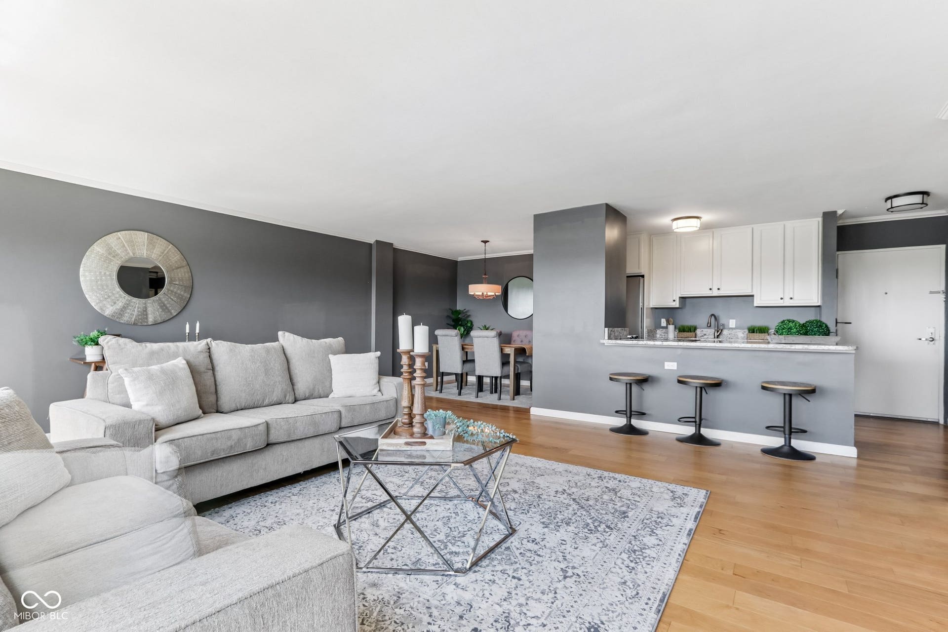 Open-concept living area featuring wood-finish flooring, a kitchen with white cabinetry, a breakfast bar, and a dining area with a chandelier
