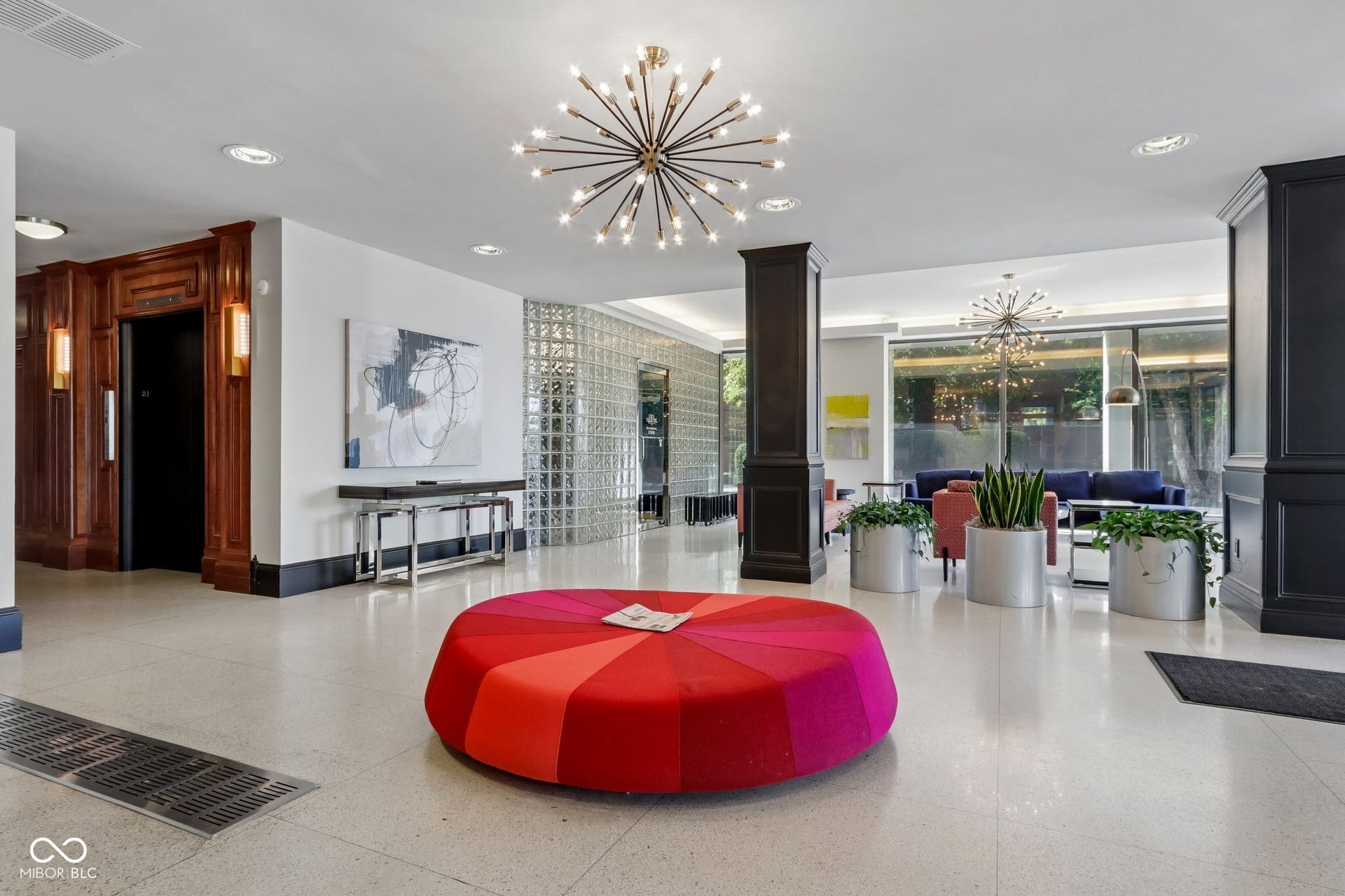 West building Lobby: Spacious lobby featuring terrazzo flooring, modern sputnik chandeliers, glass block partition, and wood-paneled elevator surround