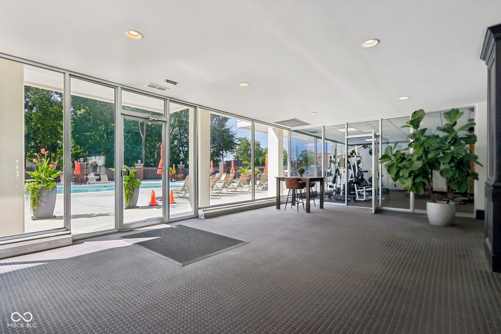 East building: Indoor-outdoor common area featuring expansive glass walls, recessed lighting, and direct access to an outdoor pool