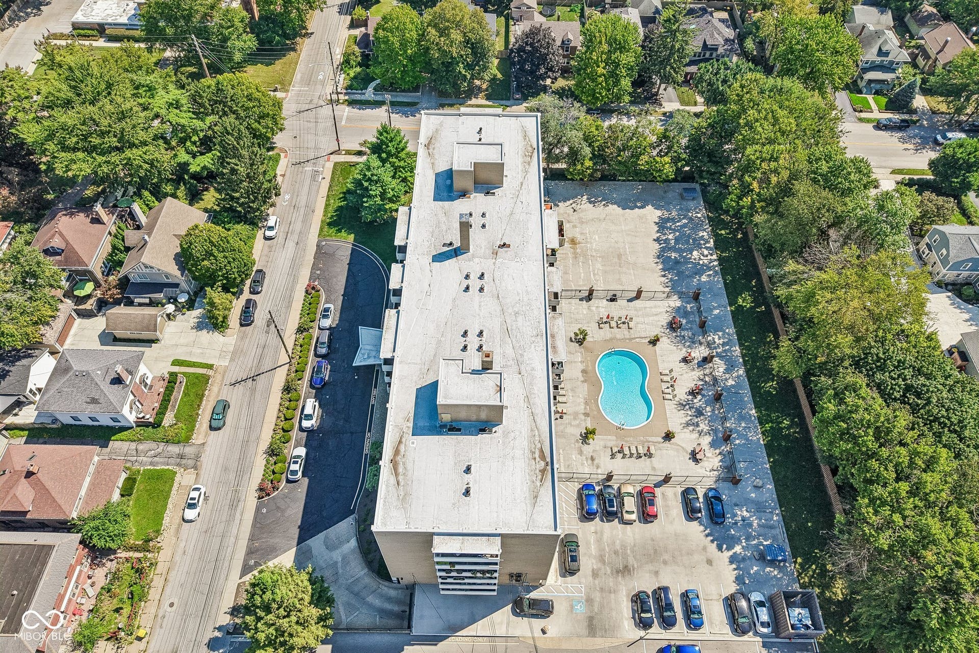 East Building: Expansive outdoor pool area with surrounding patio, a dedicated parking lot, and mature perimeter trees