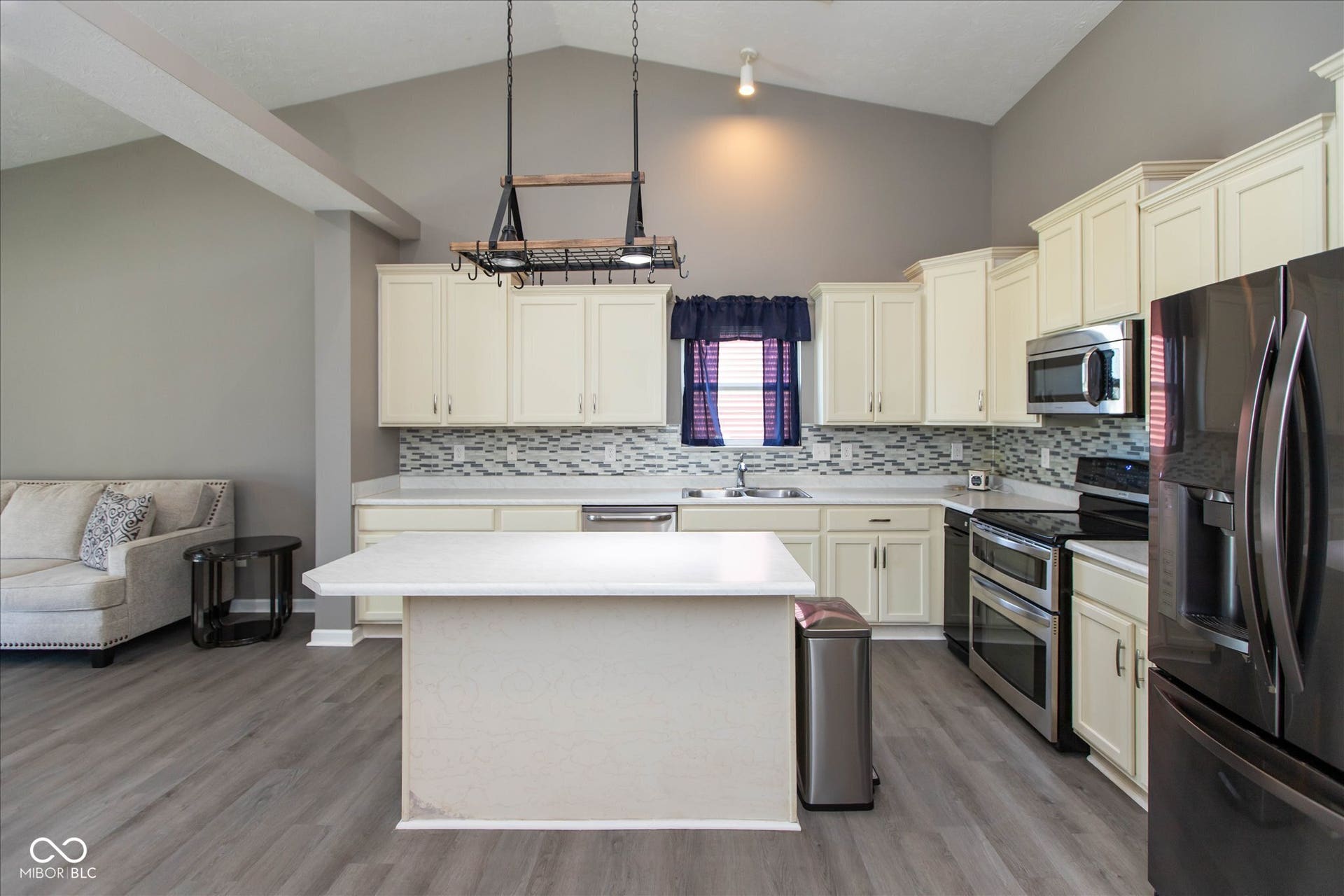 Kitchen featuring vaulted ceilings, white cabinetry, a central island, stainless steel appliances, and wood-finish flooring