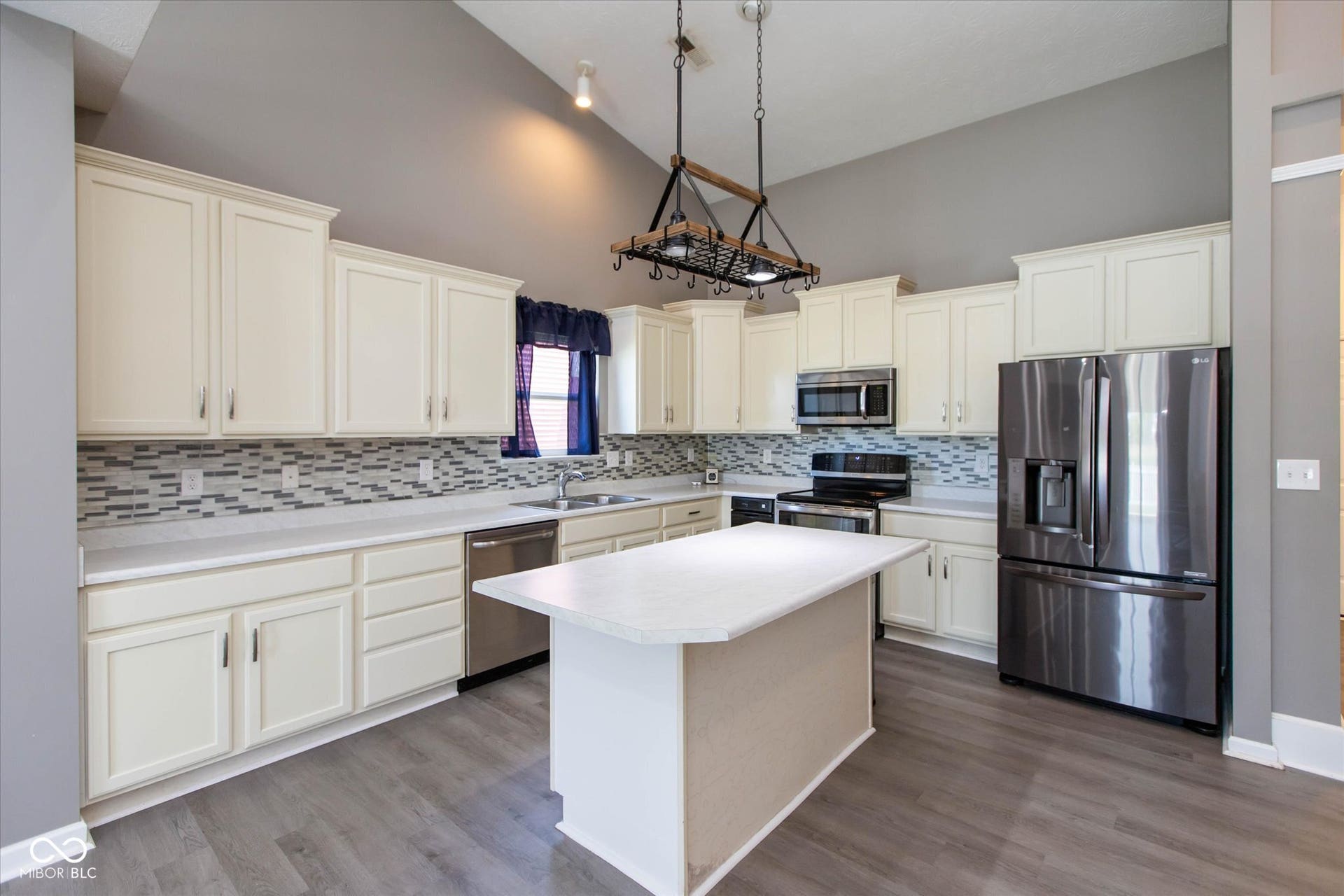 Kitchen featuring vaulted ceilings, a central island with a solid surface countertop, cream-colored cabinetry, stainless steel appliances, and wood-finish flooring