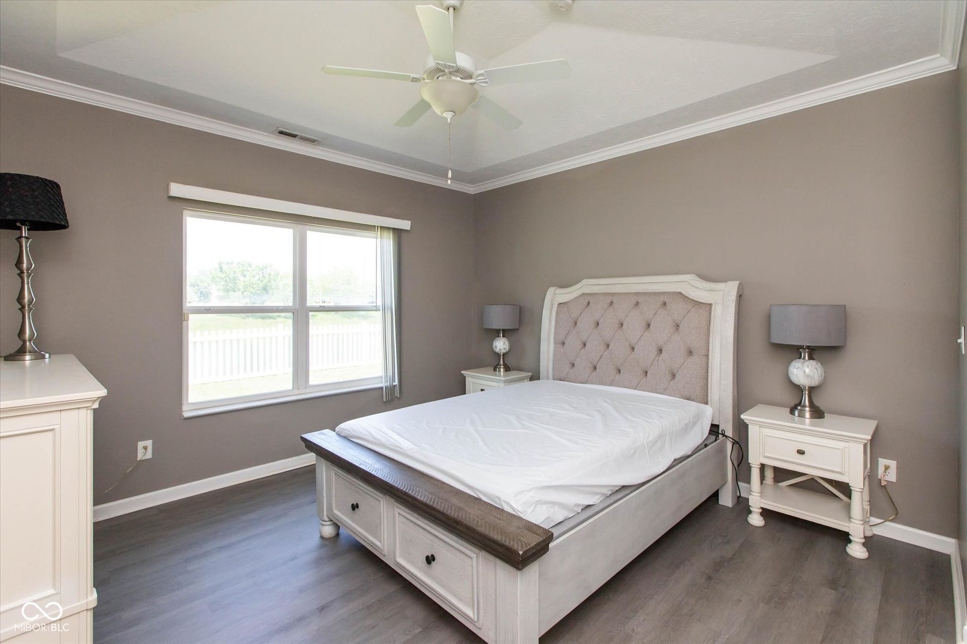 Spacious room featuring wood-finish flooring, a tray ceiling with a ceiling fan, and crown molding