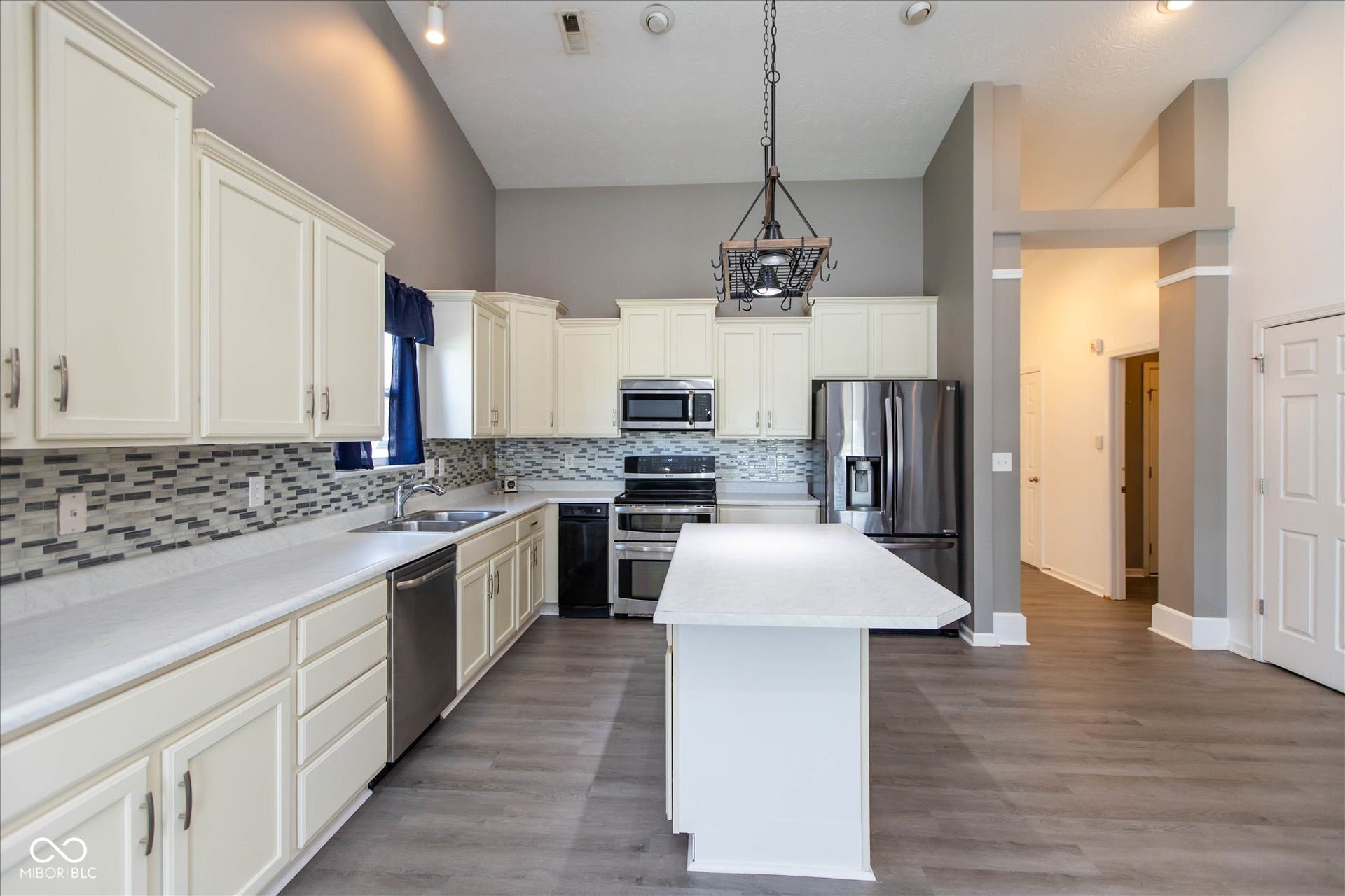 Spacious kitchen featuring cream cabinetry, stainless steel appliances, a mosaic tile backsplash, an island with counter seating, and wood-finish flooring