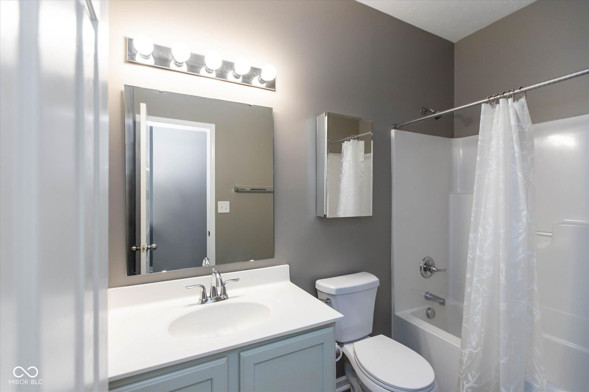 Bathroom featuring a light blue vanity, white countertop with integrated sink, chrome faucet, and a large wall-mounted mirror
