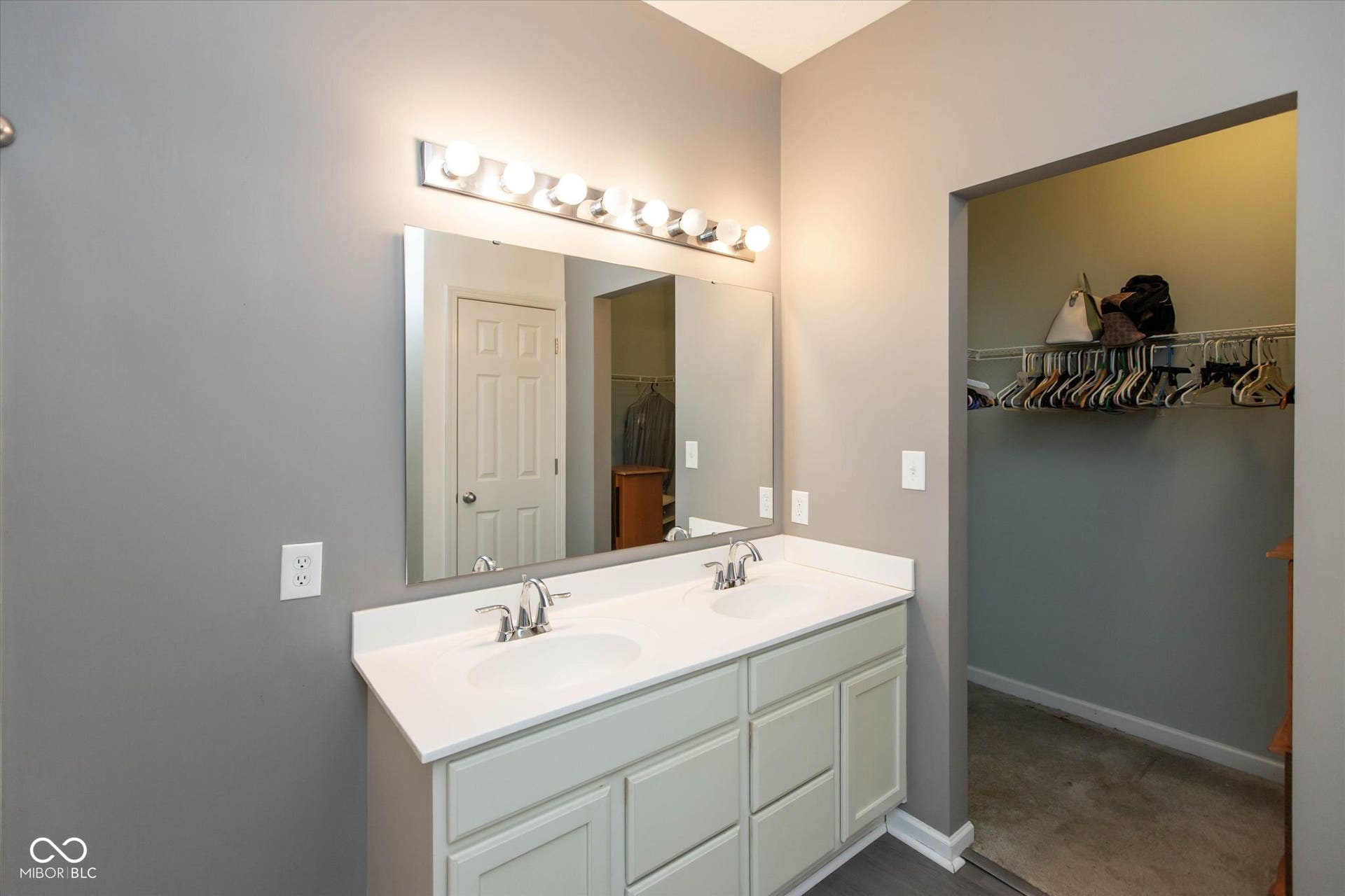 Bathroom vanity with dual sinks, white countertop, and light-colored cabinetry