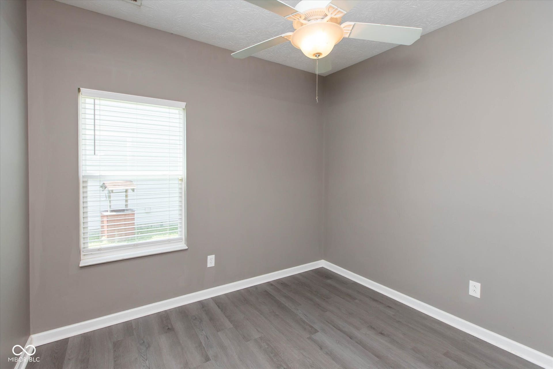 Neutral-toned room featuring wood-finish flooring, a ceiling fan with integrated lighting, and a single window with blinds