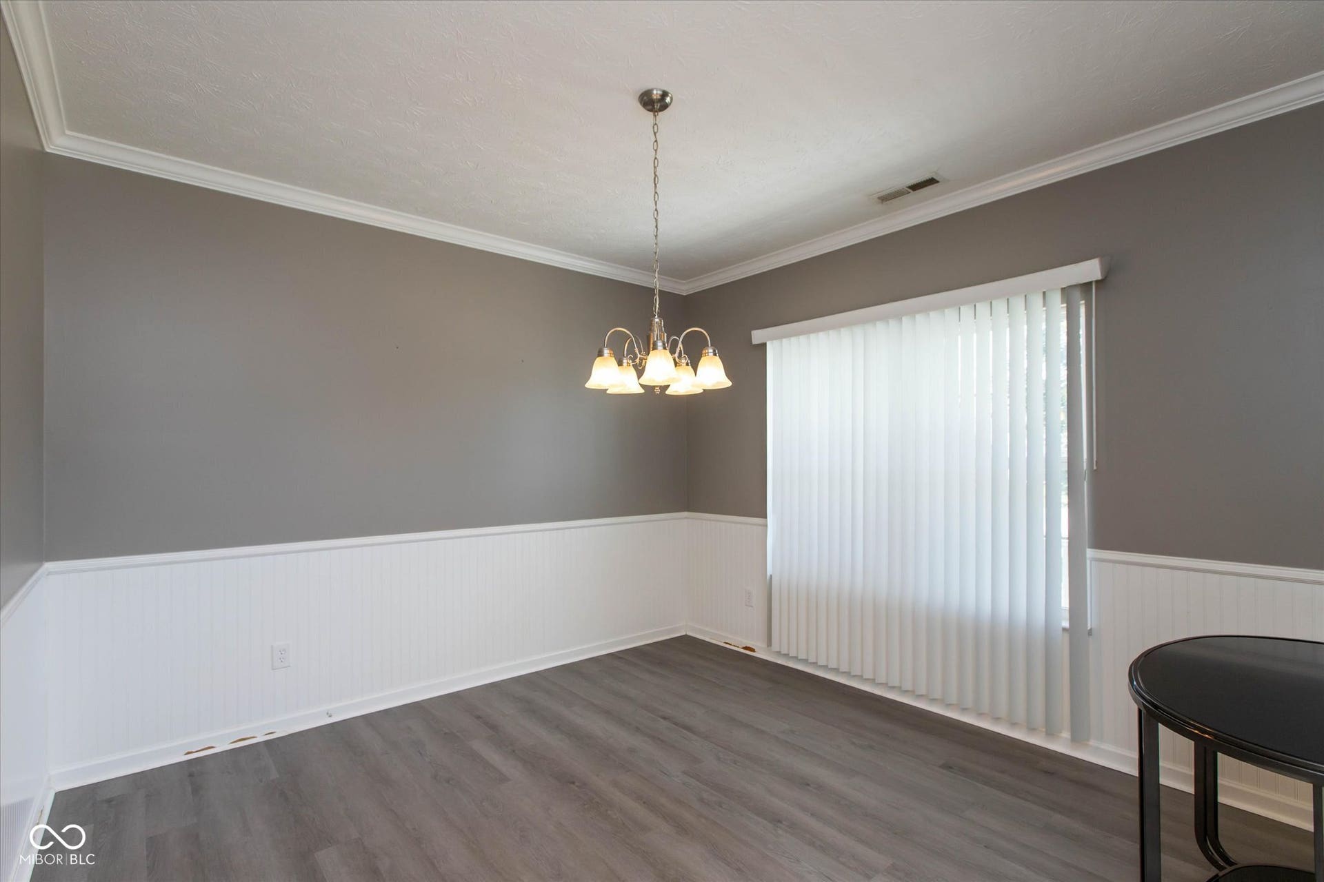 Spacious room featuring wood-finish flooring, two-tone wall paint, white wainscoting, and crown molding