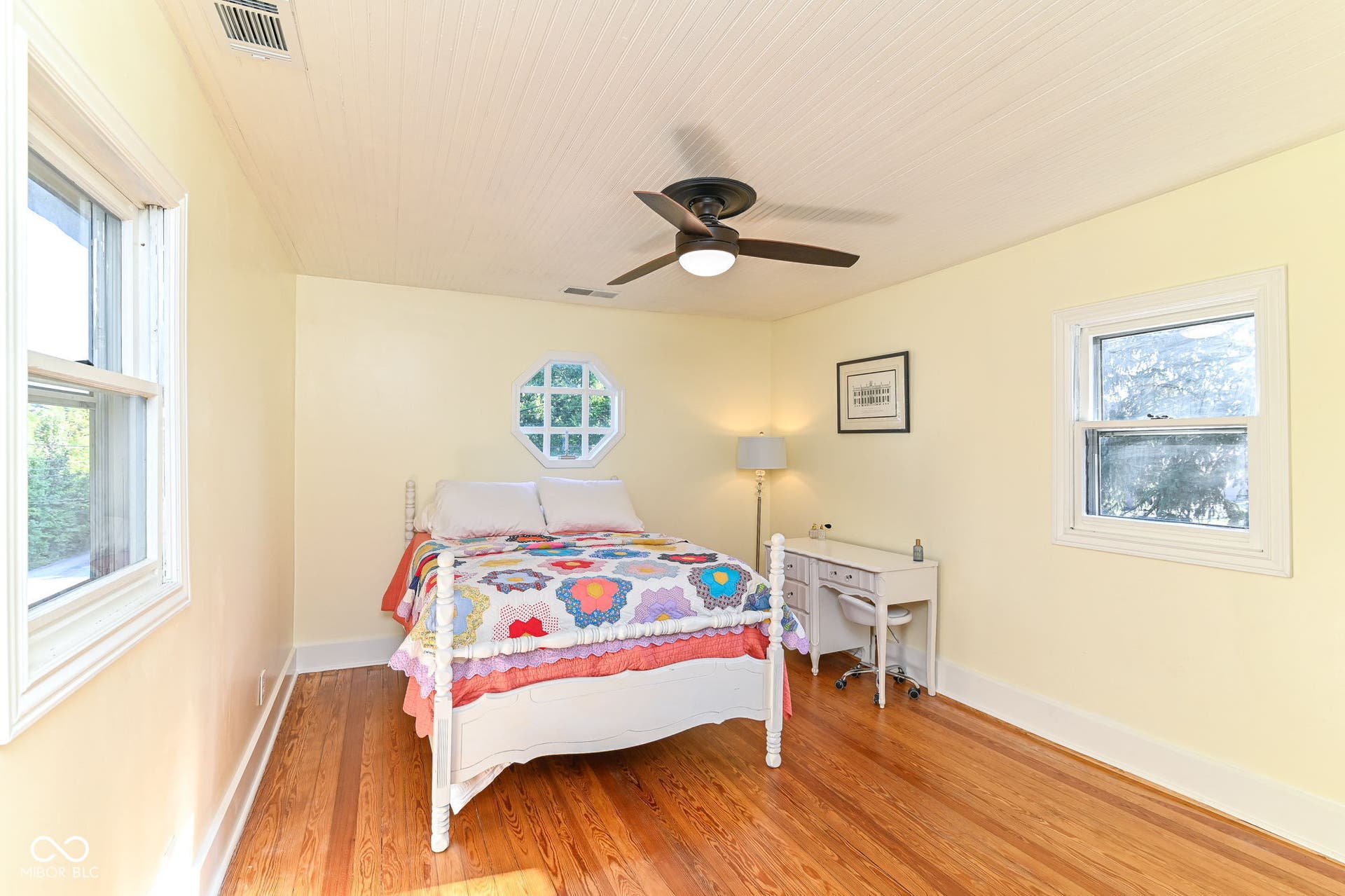 Bright additional bedroom with original pine floors, beadboard ceiling, ceiling fan and windows on multiple sides.