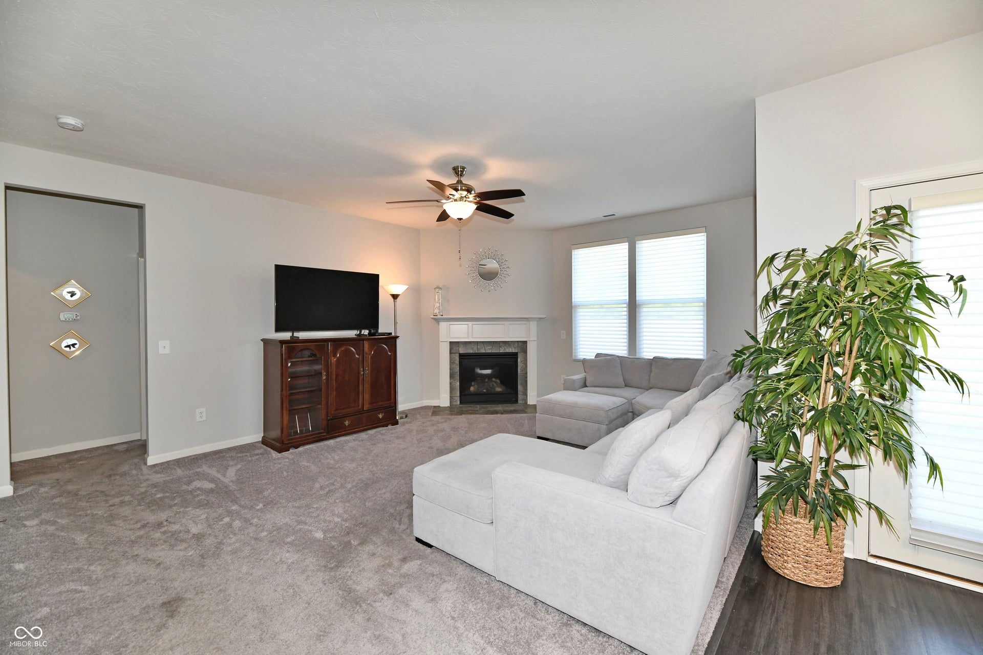 Carpeted living area with a ceiling fan, a gas log fireplace with a white mantel