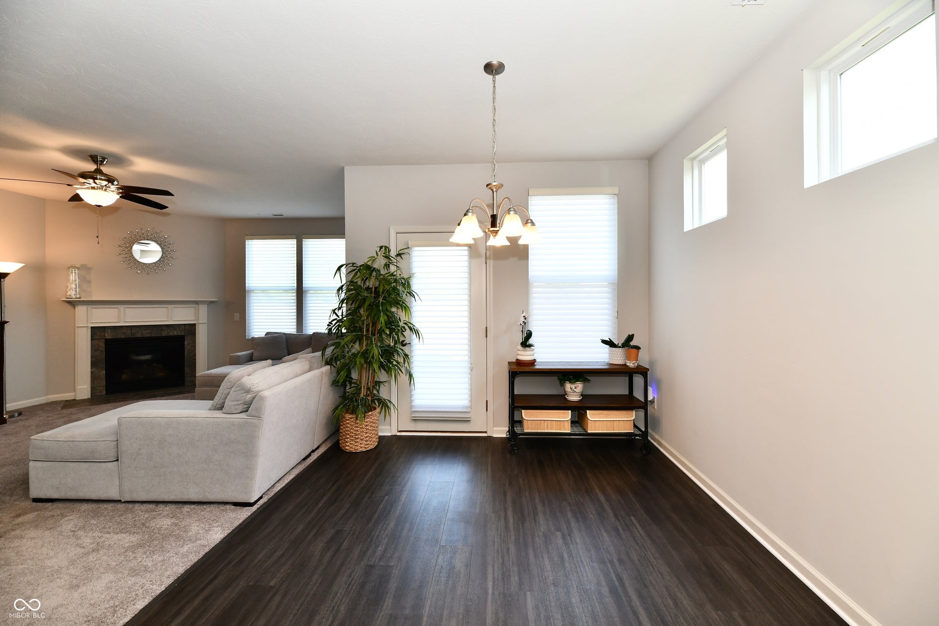 Recessed fireplace with a light-colored mantel, ceiling fan with integrated lighting, wood-finish flooring