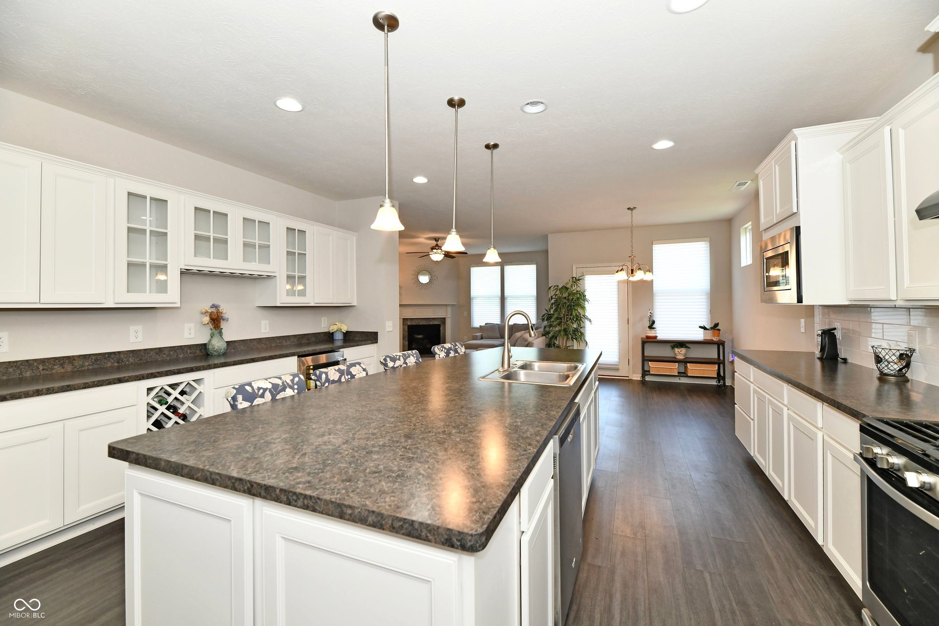 Spacious kitchen featuring an extended island with a built-in sink, white cabinetry with glass-front accents, dark wood-finish flooring, and recessed lighting