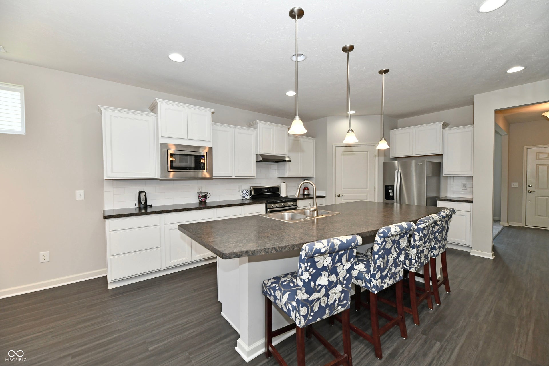 White cabinetry, stainless steel appliances, dark countertops, wood-finish flooring, and recessed lighting