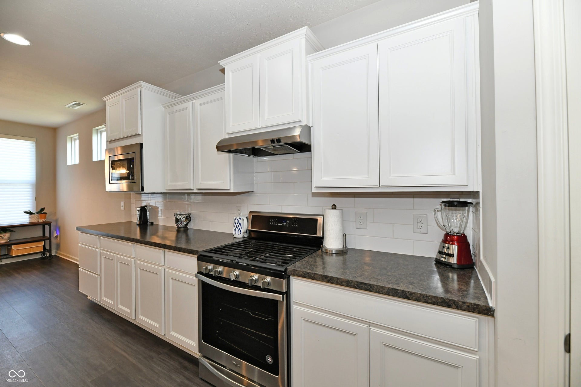 White shaker-style cabinetry with crown molding, stainless steel appliances, dark countertops, white subway tile backsplash, and wood-finish flooring