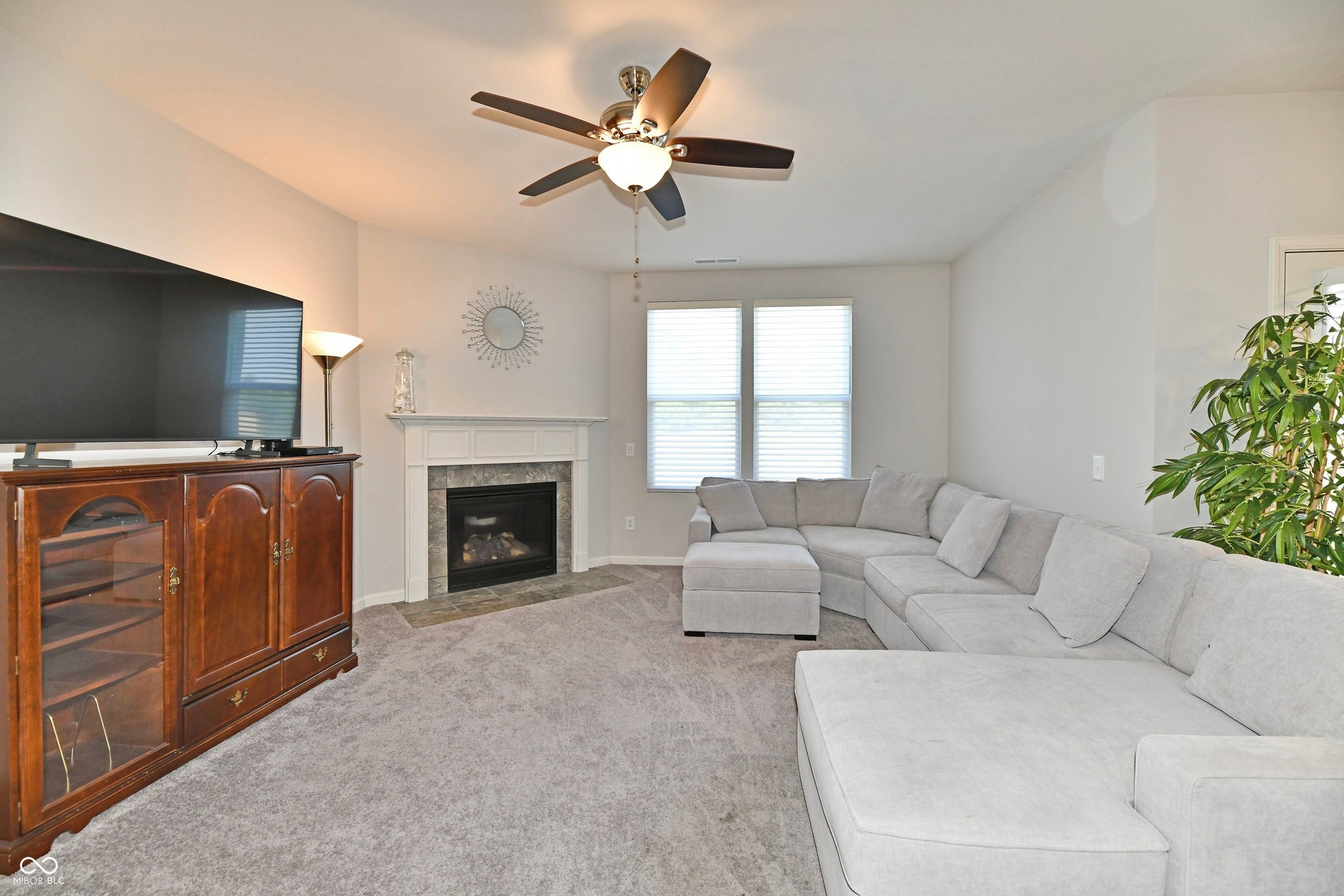 Vaulted ceiling with a ceiling fan, fireplace with a tiled surround, white mantel, and two windows with blinds