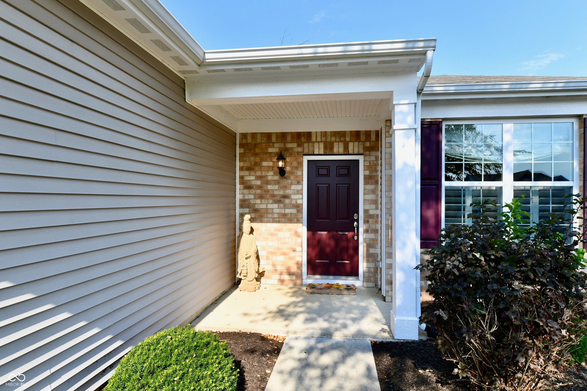 Entry featuring a brick facade, covered porch, dark paneled door, and exterior sconce lighting