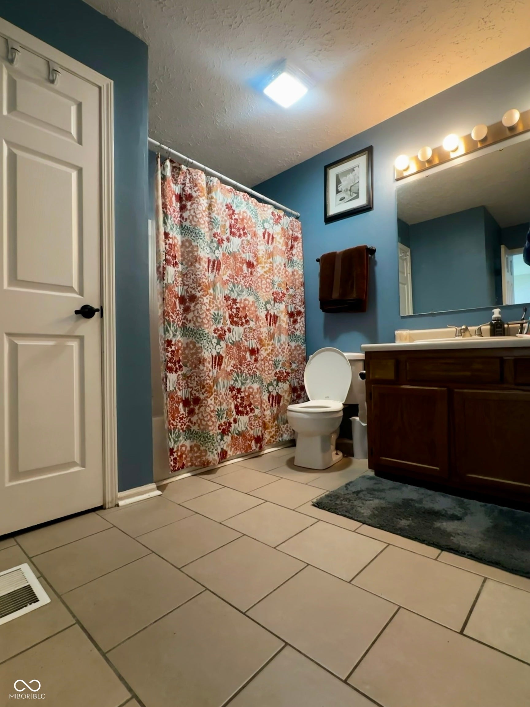 Tile flooring, vanity with wood-finish cabinetry, and a full bathtub with shower