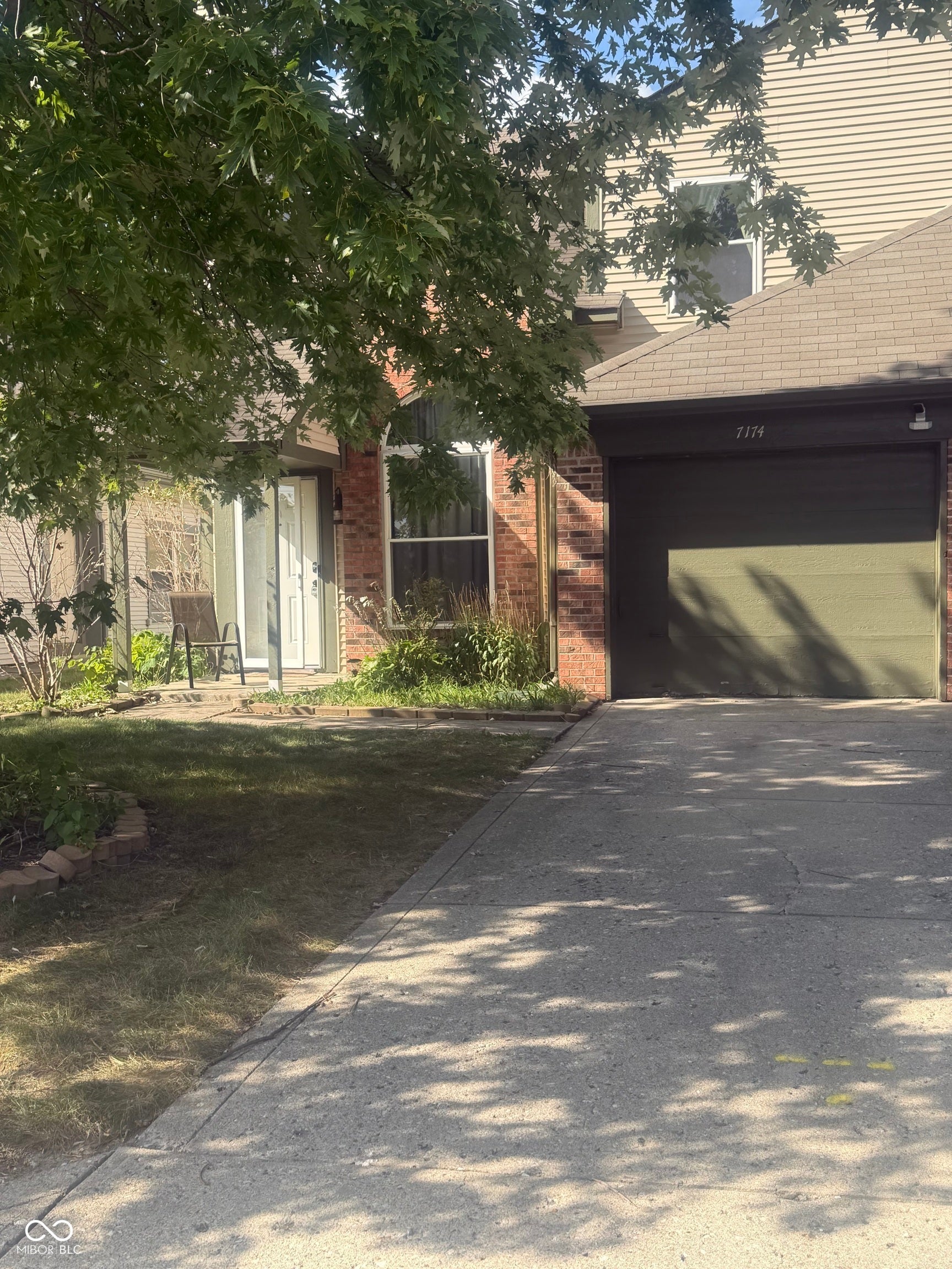 Brick and siding exterior with an attached garage, concrete driveway, and established trees