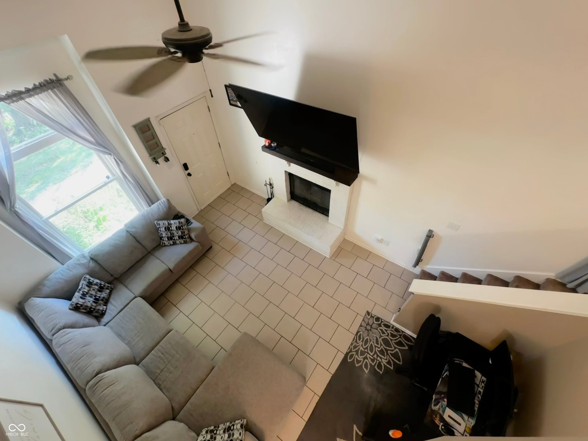 Tile flooring, corner fireplace, staircase with carpeted treads, ceiling fan, and large window