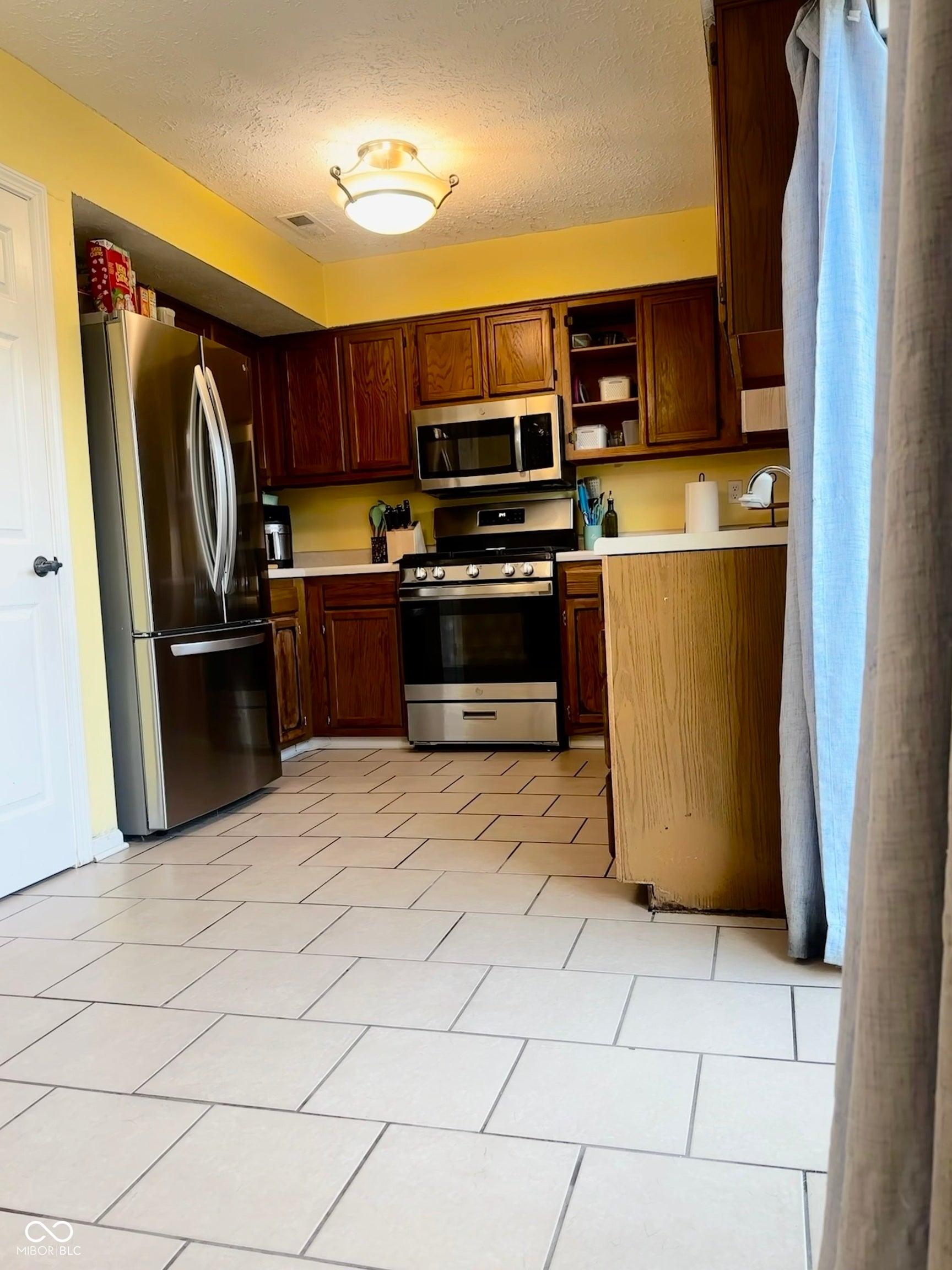 Kitchen featuring stainless steel appliances, wood-finish cabinetry, light-toned countertop surfaces, and tile flooring