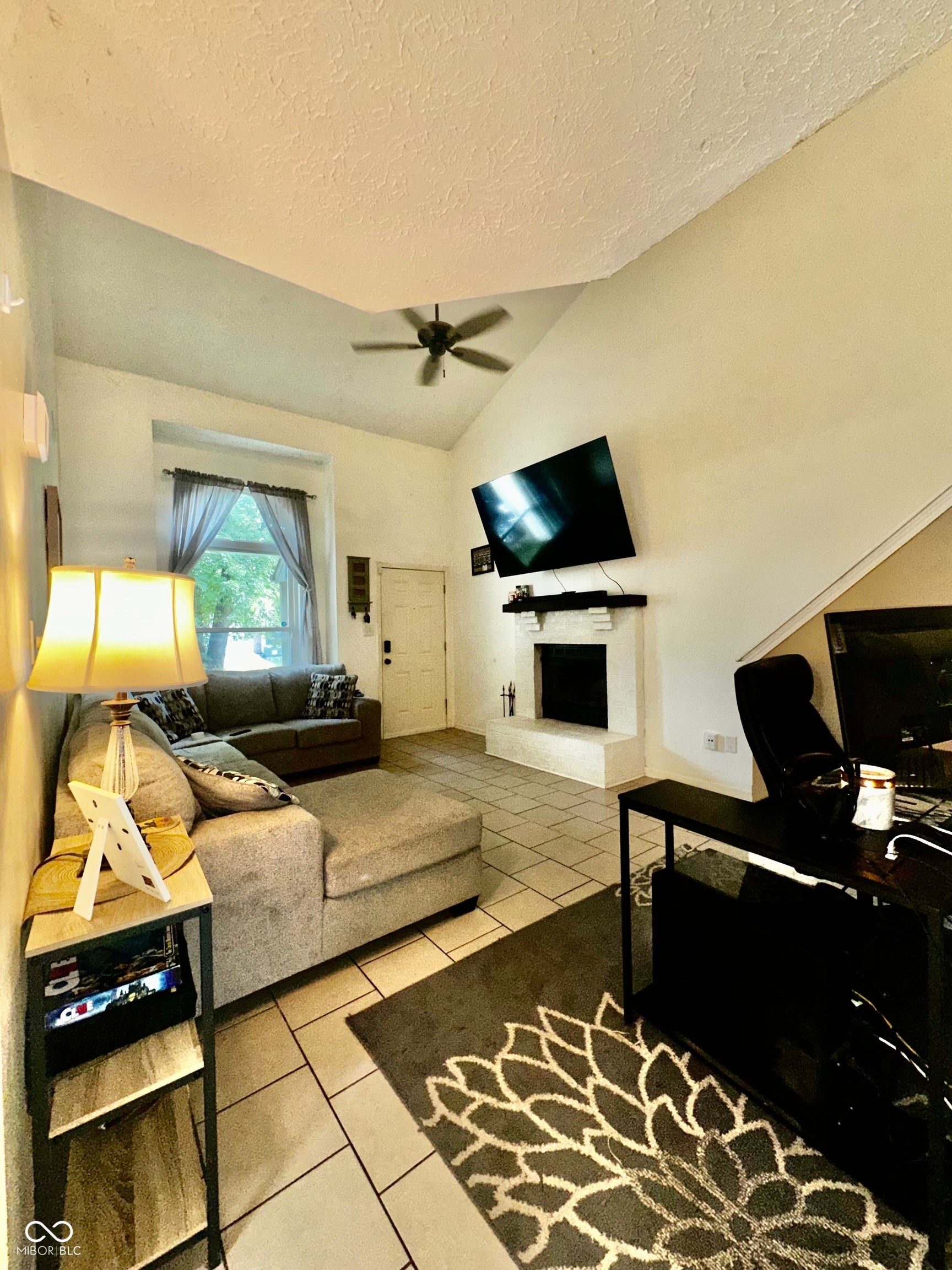Vaulted ceiling with ceiling fan, tile flooring, and a built-in fireplace