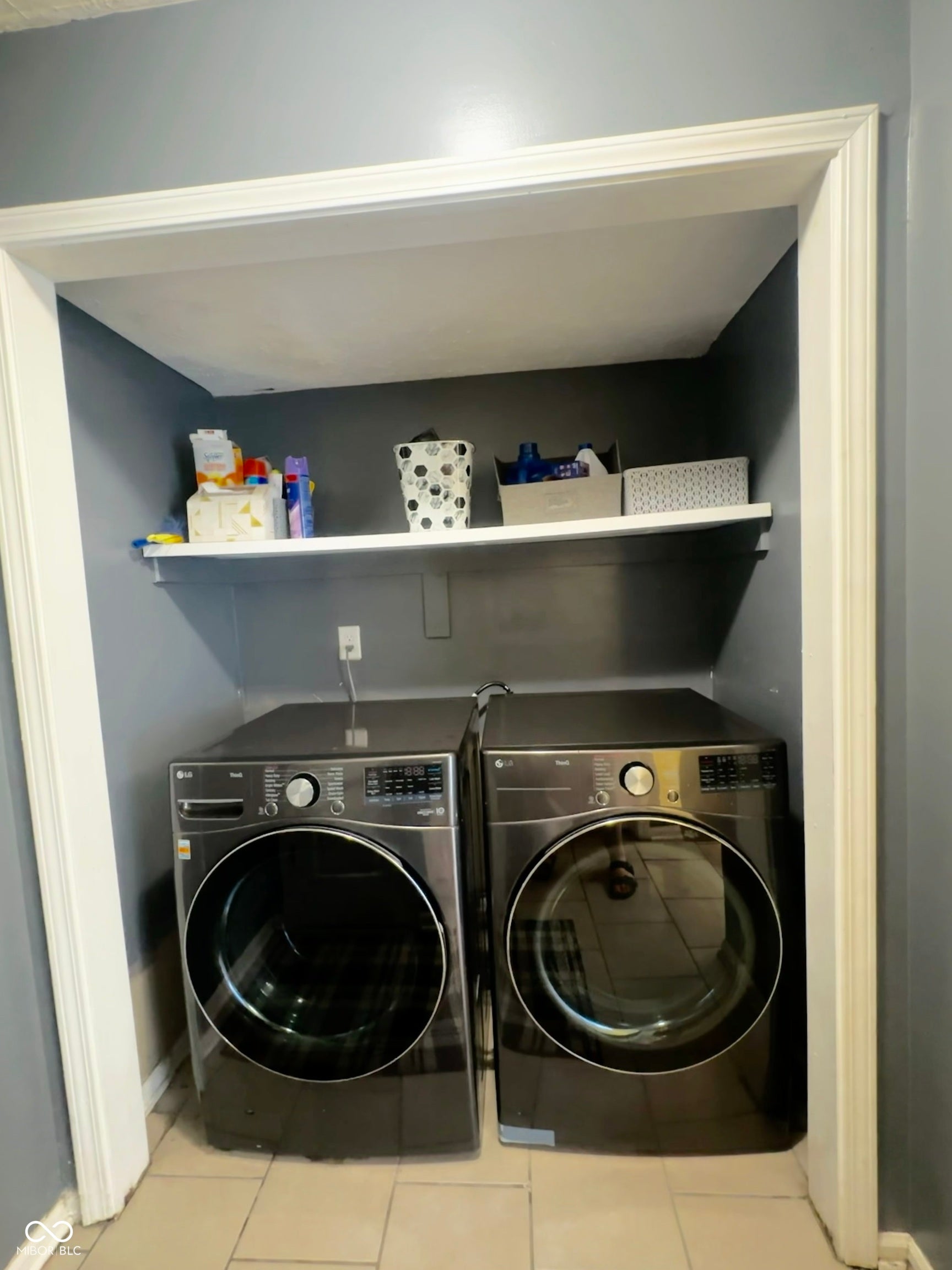 Integrated laundry area with tile flooring and a built-in storage shelf