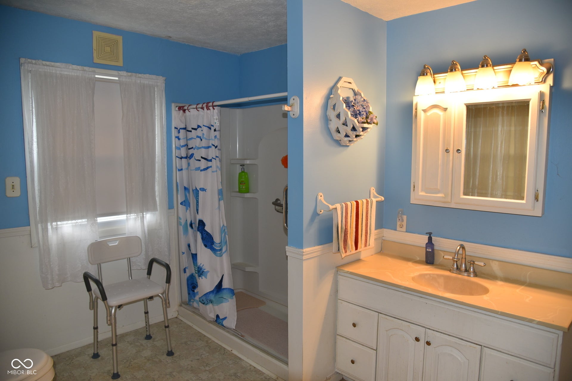 Bathroom featuring a single window, white paneled lower walls, a built-in vanity with an integrated sink, and a medicine cabinet with an overhead light fixture
