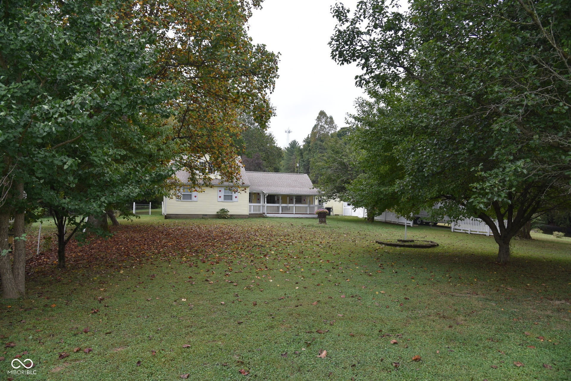 Expansive lawn with mature trees, a light-colored exterior, and a covered porch