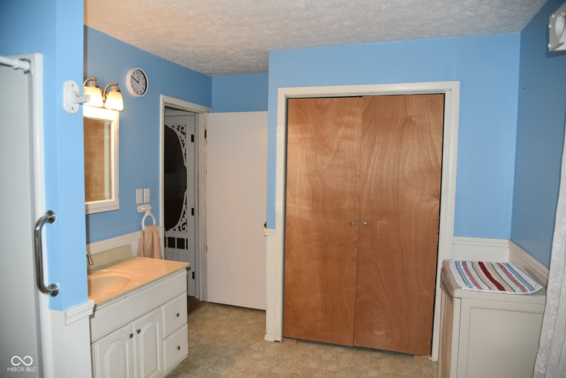 Bathroom featuring a vanity with integrated sink, wood-finish bi-fold closet doors, and wainscoting