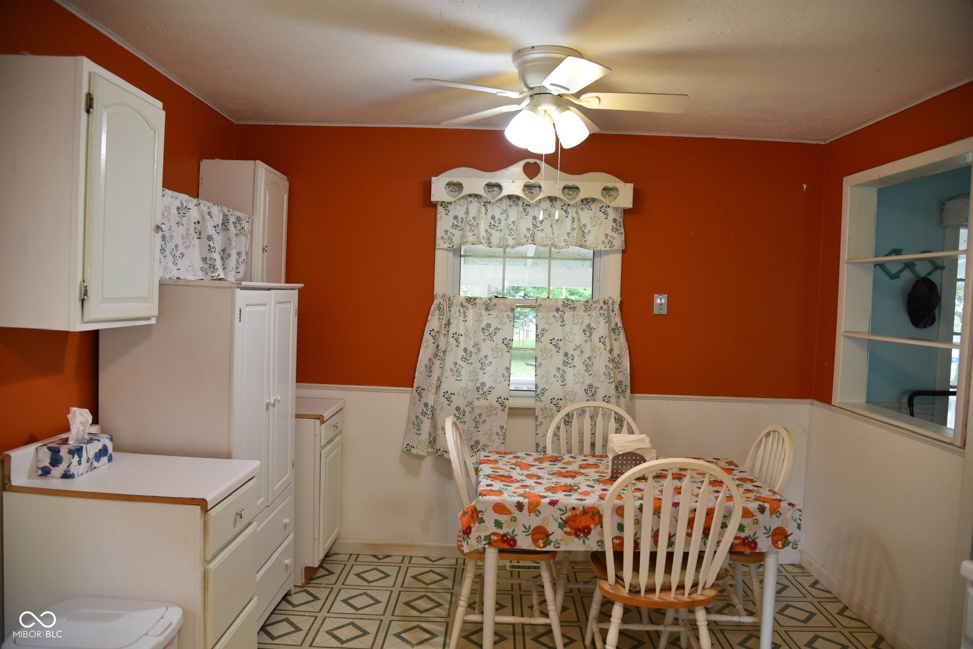 White cabinetry, patterned flooring, ceiling fan with integrated lighting, a framed window, and a pass-through window with shelving