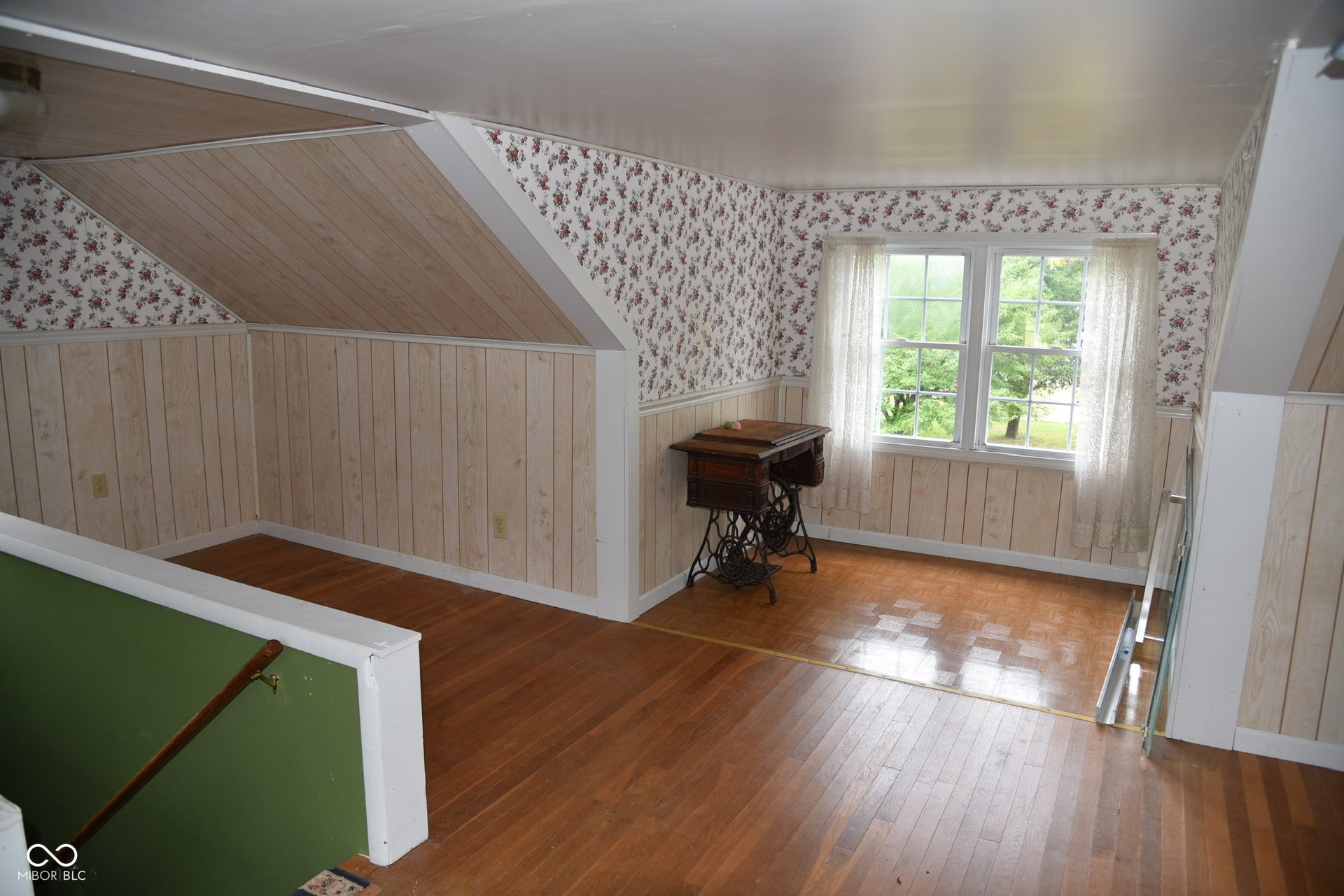 Hardwood flooring, paneled wall accents, dual windows, and sloped ceiling details