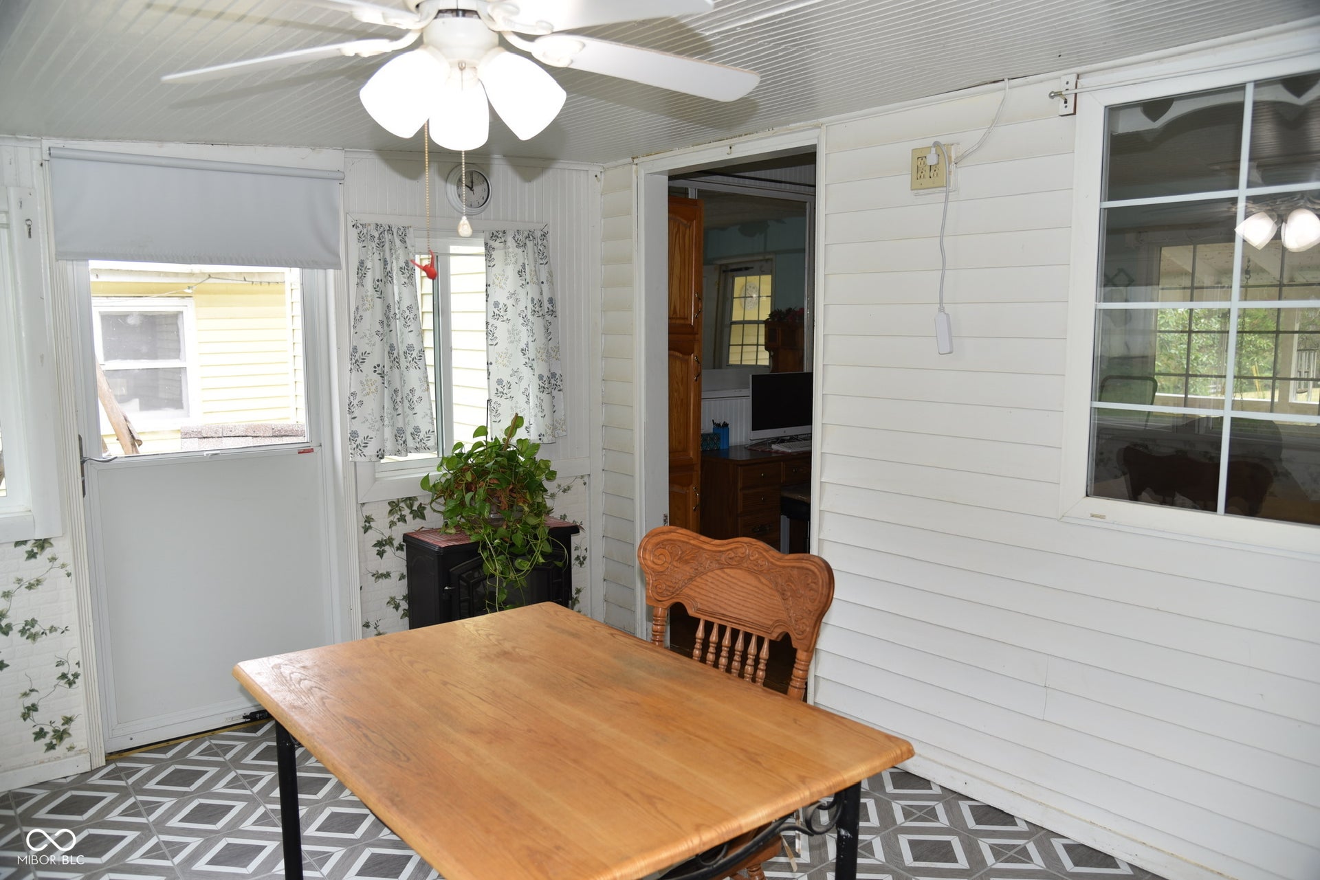 Enclosed porch featuring a ceiling fan, white paneled walls, multiple windows, and patterned tile flooring