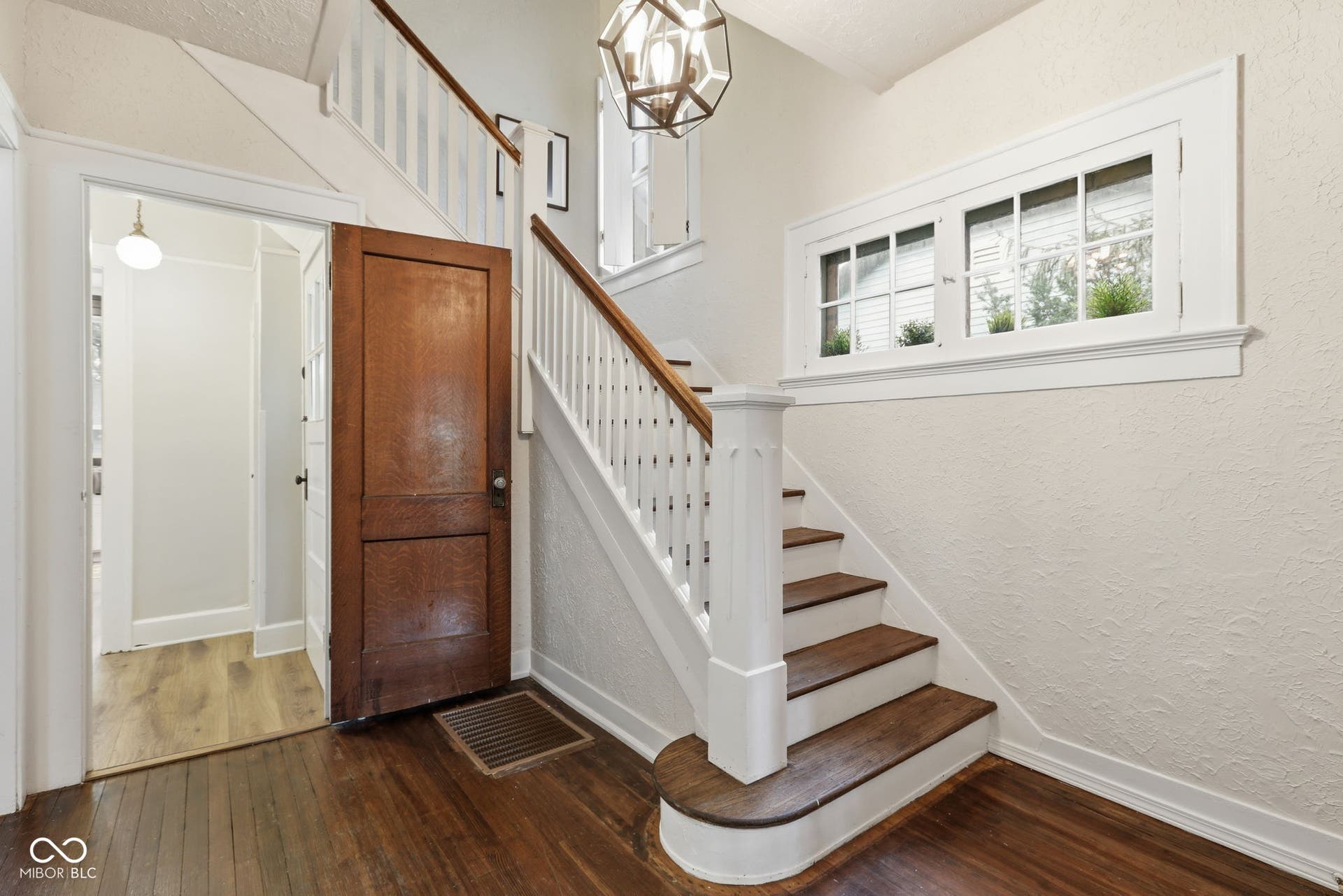 Hardwood flooring throughout, a classic white balustrade staircase with dark wood treads, and a geometric pendant light fixture