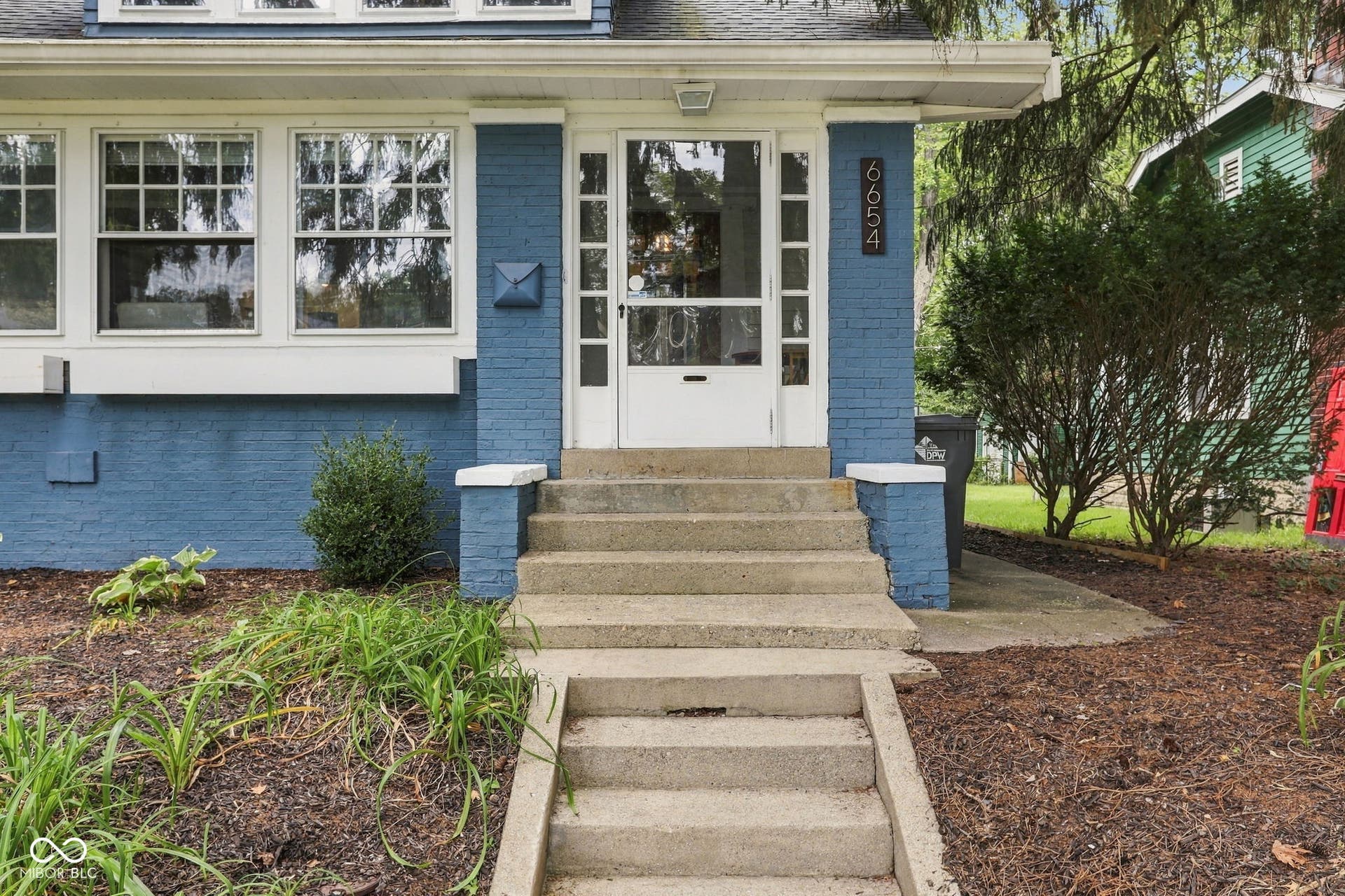 Blue brick exterior with white trim, multi-pane windows, and concrete steps