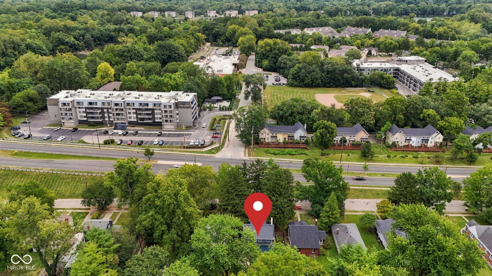 Residential property surrounded by mature trees, with a nearby multi-story apartment building and a baseball field