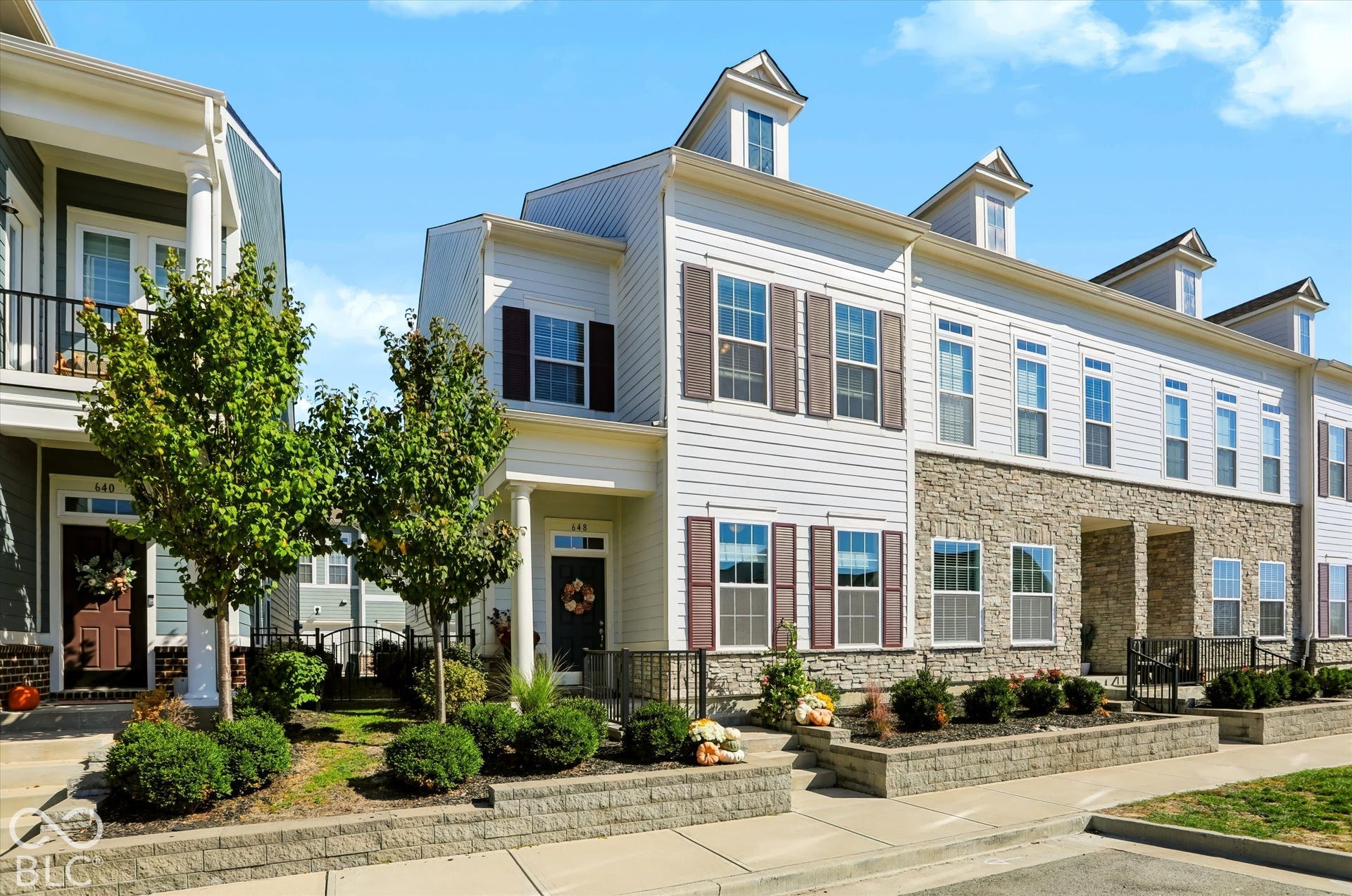 White siding exterior with stone accent, dormer windows, decorative shutters, and established landscaping