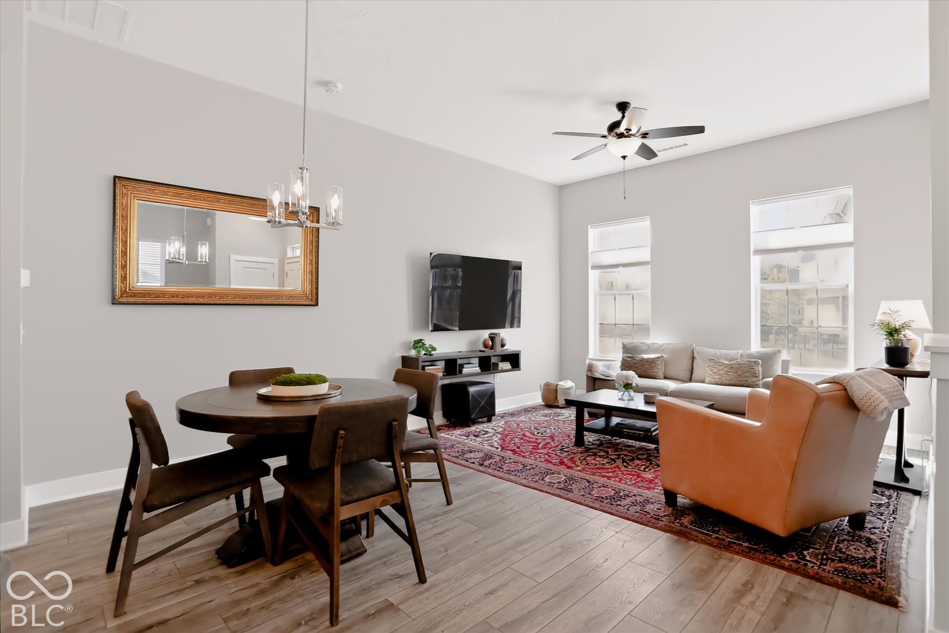 Wood-finish flooring, two large windows, ceiling fan with integrated lighting, recessed lighting, and a modern chandelier