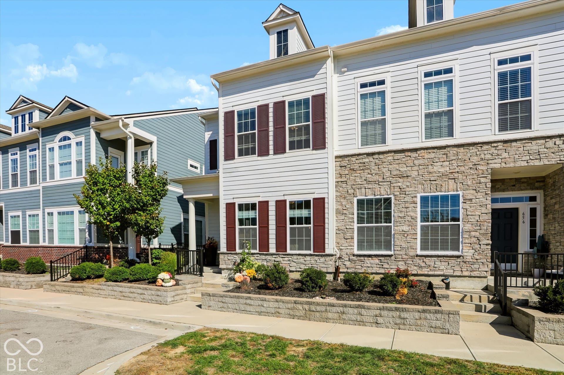 Stone facade with siding accents, decorative window shutters, multiple dormer windows, and a manicured landscape with retaining walls